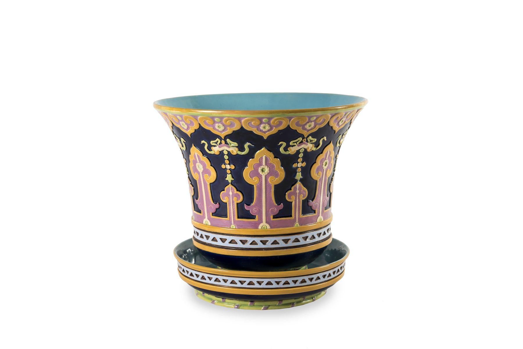 This wonderful cache-pot was made by the British manufacturer Minton. Its belly is decorated with stylised and colourful vegetal motifs typical of the palette of this manufacture. The base of the planter is decorated with a frieze of triangles