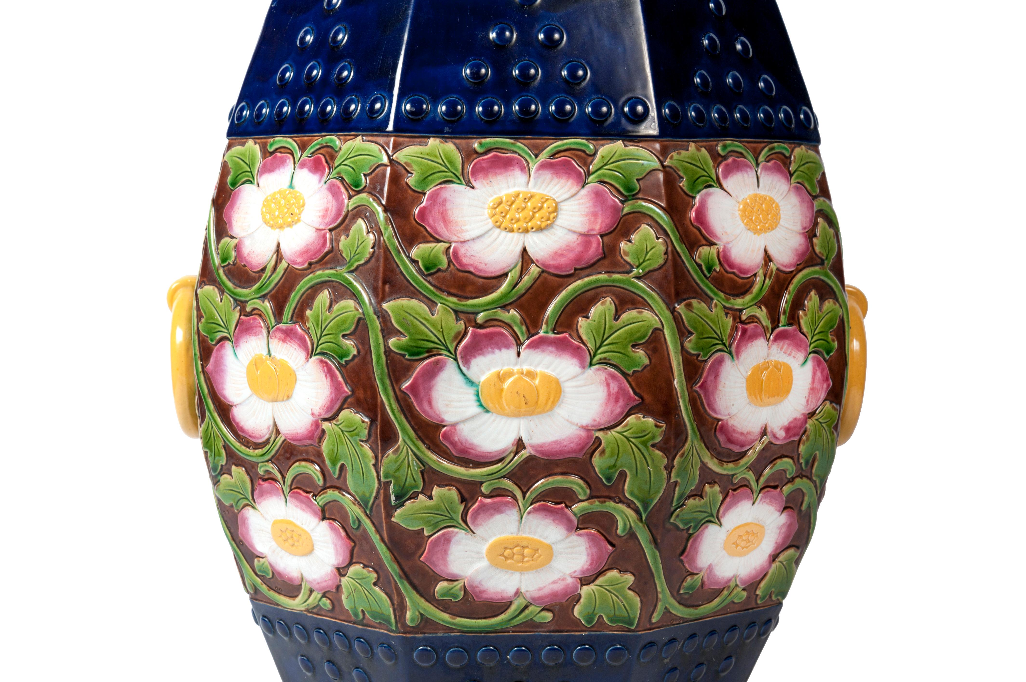 This superb garden seat or garden stool is the work of the British manufacturer Minton. Its inventive facetted drum shape is decorated with flowers on a brown background. The large, burst flowers with golden buds reveal white petals with pinkish