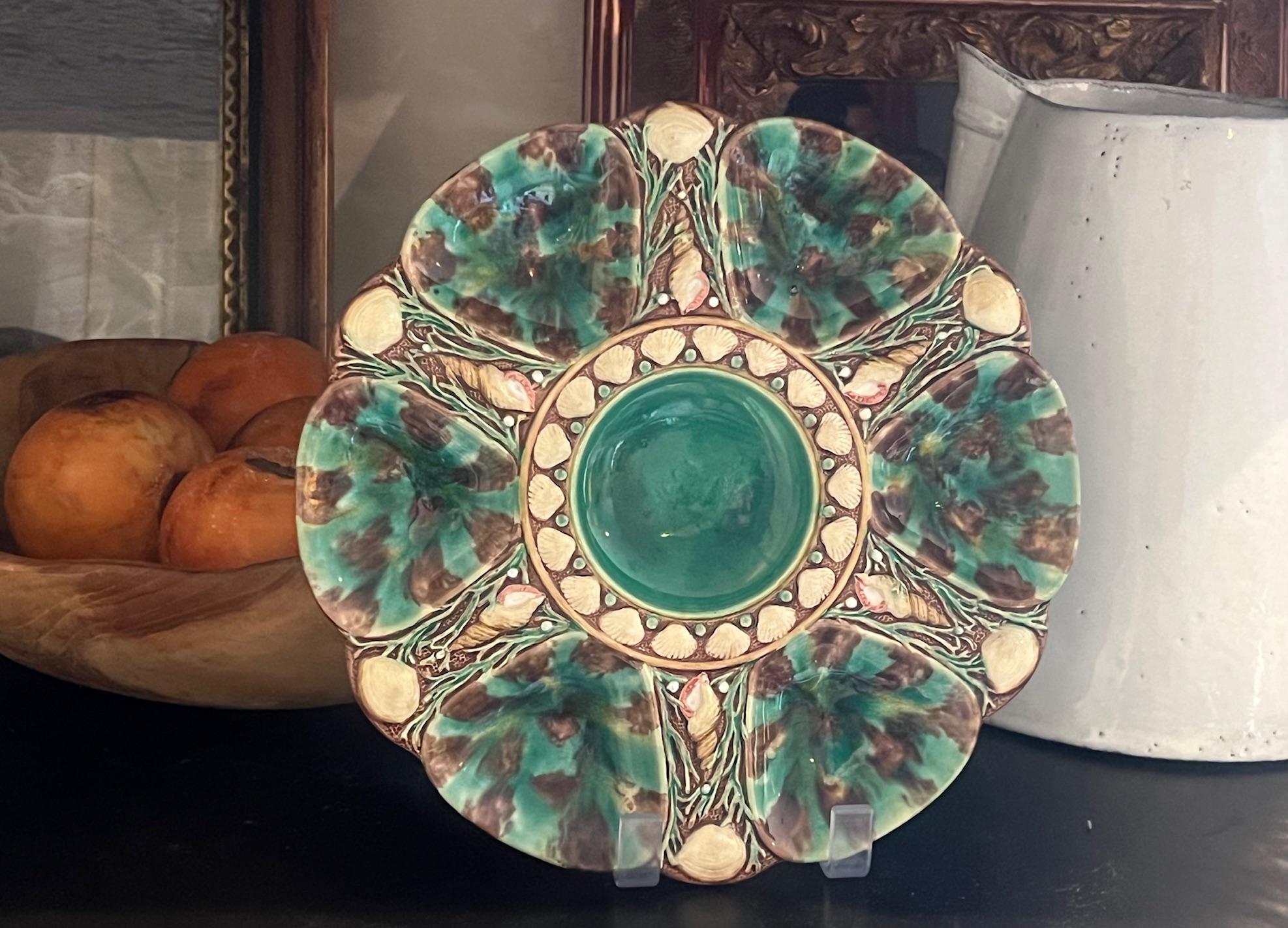 Smaragdgrüner Majolikateller, hergestellt in England von Minton im Jahr 1876. Sechs Brunnen sind handbemalt und von Muscheln und Seetang umgeben. Die mittlere Vertiefung kann für Zitronenspalten oder eine Minette verwendet werden.

Die Rückseite ist