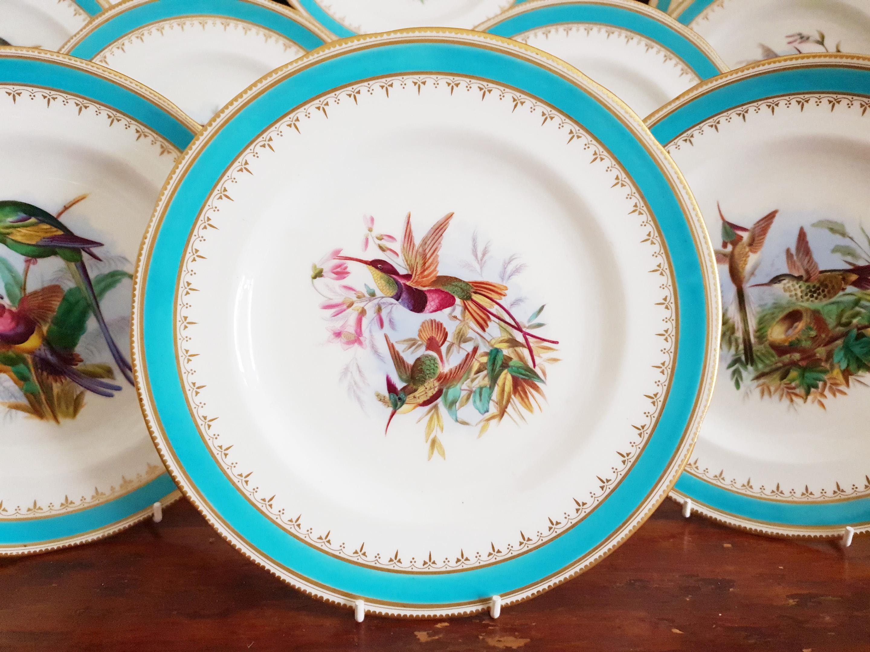 A Minton dessert service circa 1910, the plates decorated with humming birds and parrots perched on branches and flowers reserved on a white background. A turquoise border surrounds the edge within a gilt somewhat fleur de lys pattern and gilt rims.