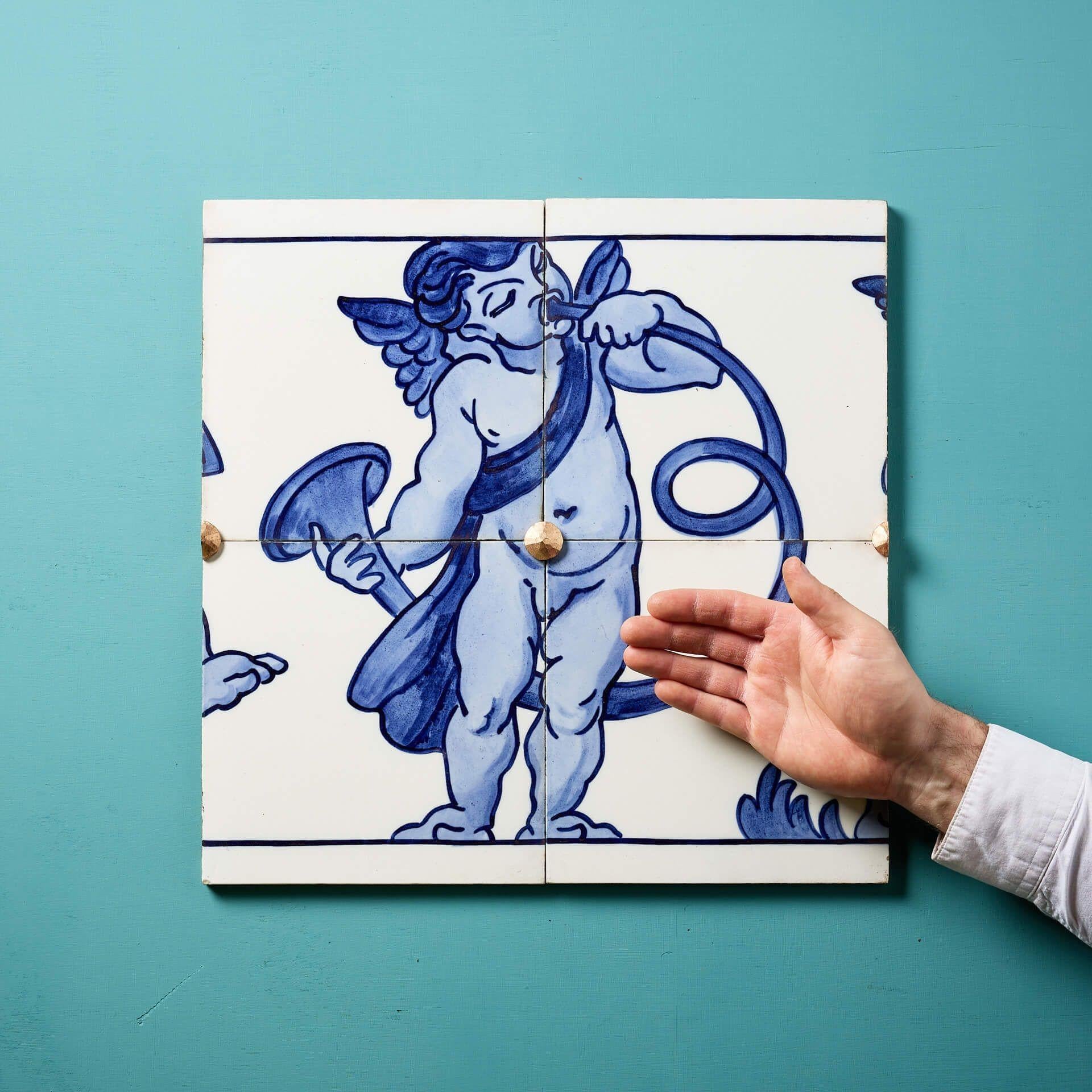 A set of 4 antique dust-pressed ceramic tiles by Minton Hollins (stamped) creating a decorative blue and white glazed frieze panel depicting a renaissance style winged cherub playing a trumpet.

Once part of a larger design, this is just one of