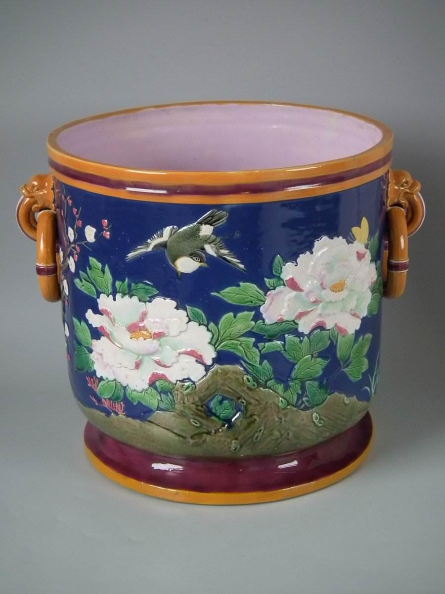 Minton Majolica jardinière which features birds of paradise and flowers amongst blossoming prunus. Minton blue ground version. Coloration: Minton-blue, ochre, puce, are predominant. The piece bears maker's marks for the Minton pottery. Bears a