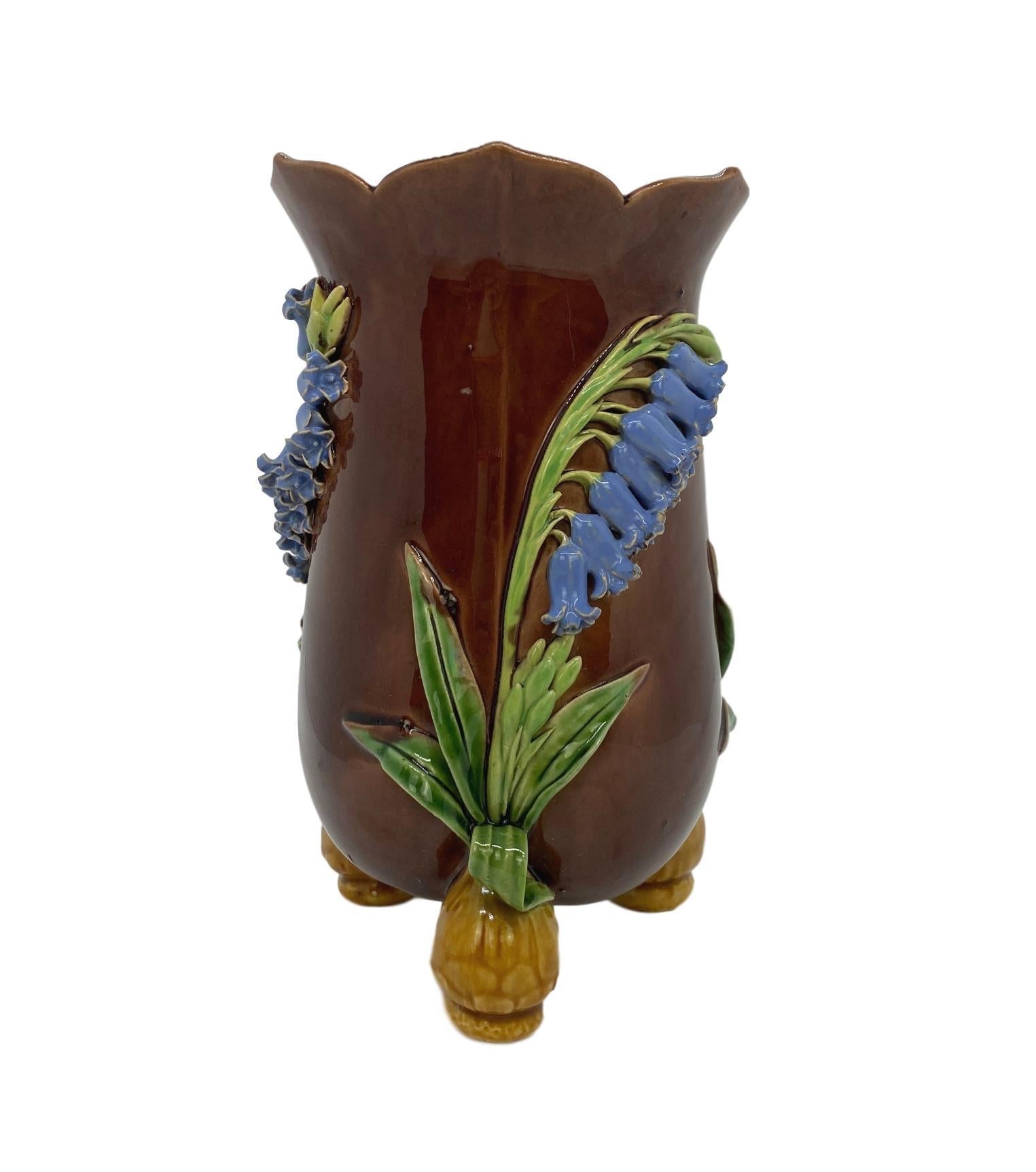 Minton Majolica vase, naturalistically modeled with applied bluebells glazed in periwinkle blue, with green stems, on a richly colored brown ground, the bulb-form feet glazed in light brown, with a periwinkle blue glazed interior, with impressed