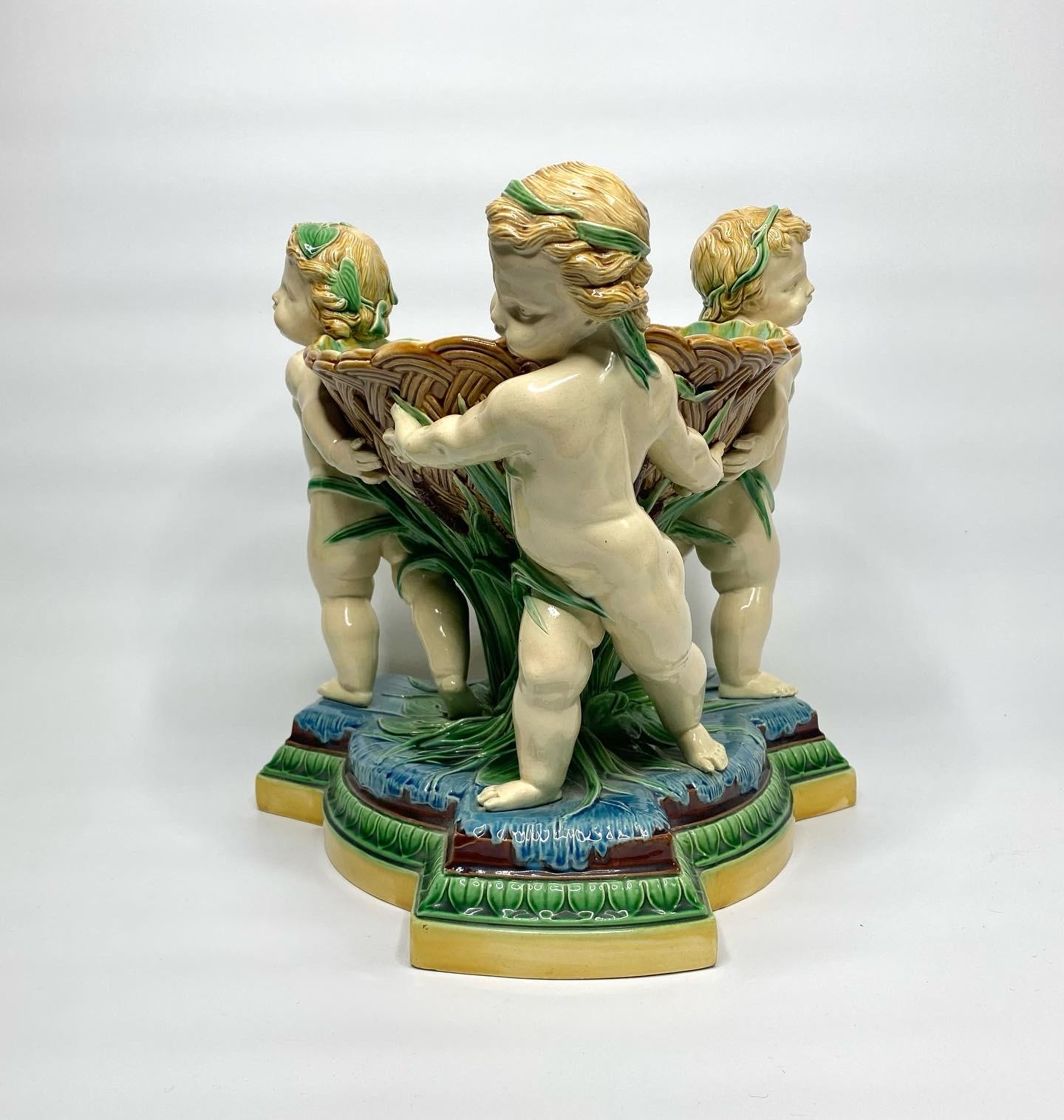 An exceptionally fine and large Minton Majolica basket, dated 1863. Modelled as three cherubs, with lily pad garlands in their hair, as they slide across a river. They carry a large weave moulded basket, supported by bulrushes, and lily pads.
The