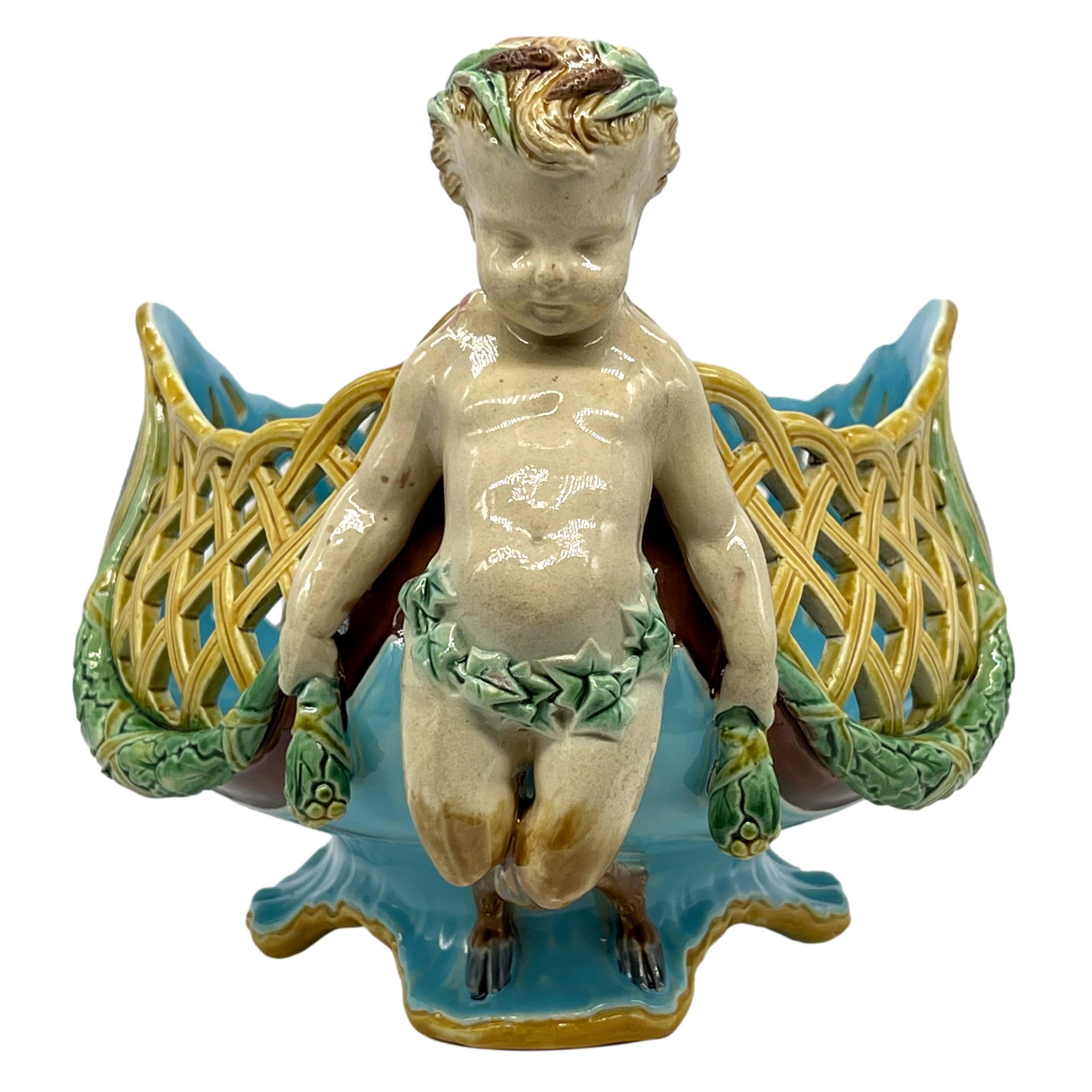 Minton Majolica Reticulated Basket Designed by Albert-Ernest Carrier-Belleuse, the lozenge-shaped body with reticulated lattice with oak garlands and oval cartouches with mottled glazing, a faun to either side wearing cattail wreaths tied in a bow