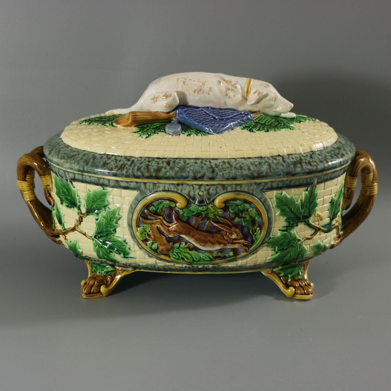 Minton Majolica game pie dish with liner which features a hunting dog asleep next to a gun, a powder flask and a game bag. Colouration: cream, green, brown, are predominant. The piece bears maker's marks for the Minton pottery. Bears a pattern
