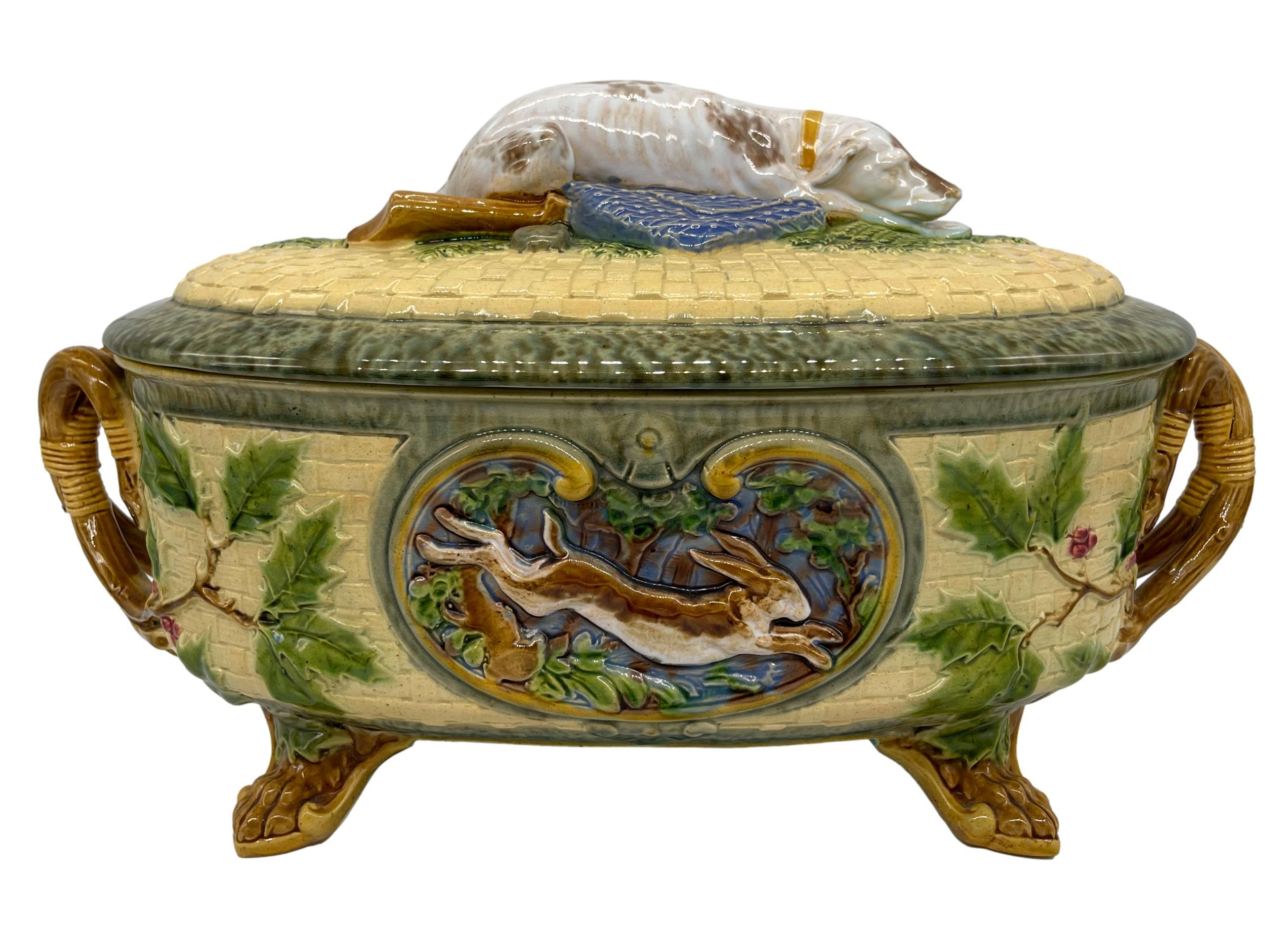 A Minton majolica two-handled game pie tureen and cover, the finial modelled as a sleeping hound recumbent on a bed of ferns, with shooting bag, gun and powder flasks, the dish molded with a pheasant within a cartouche, the reverse with a hare