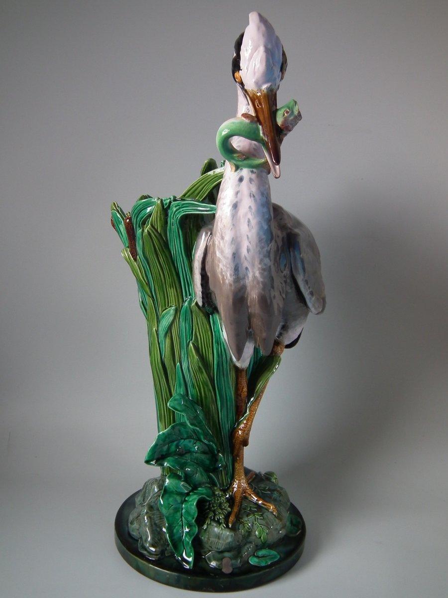 Mintons majolica stick or umbrella Stand which features a heron with fish in its mouth. Reeds and bullrushes (cattails) behind the bird form the receptacle. Coloration: green, grey, black, are predominant. The piece bears maker's marks for the