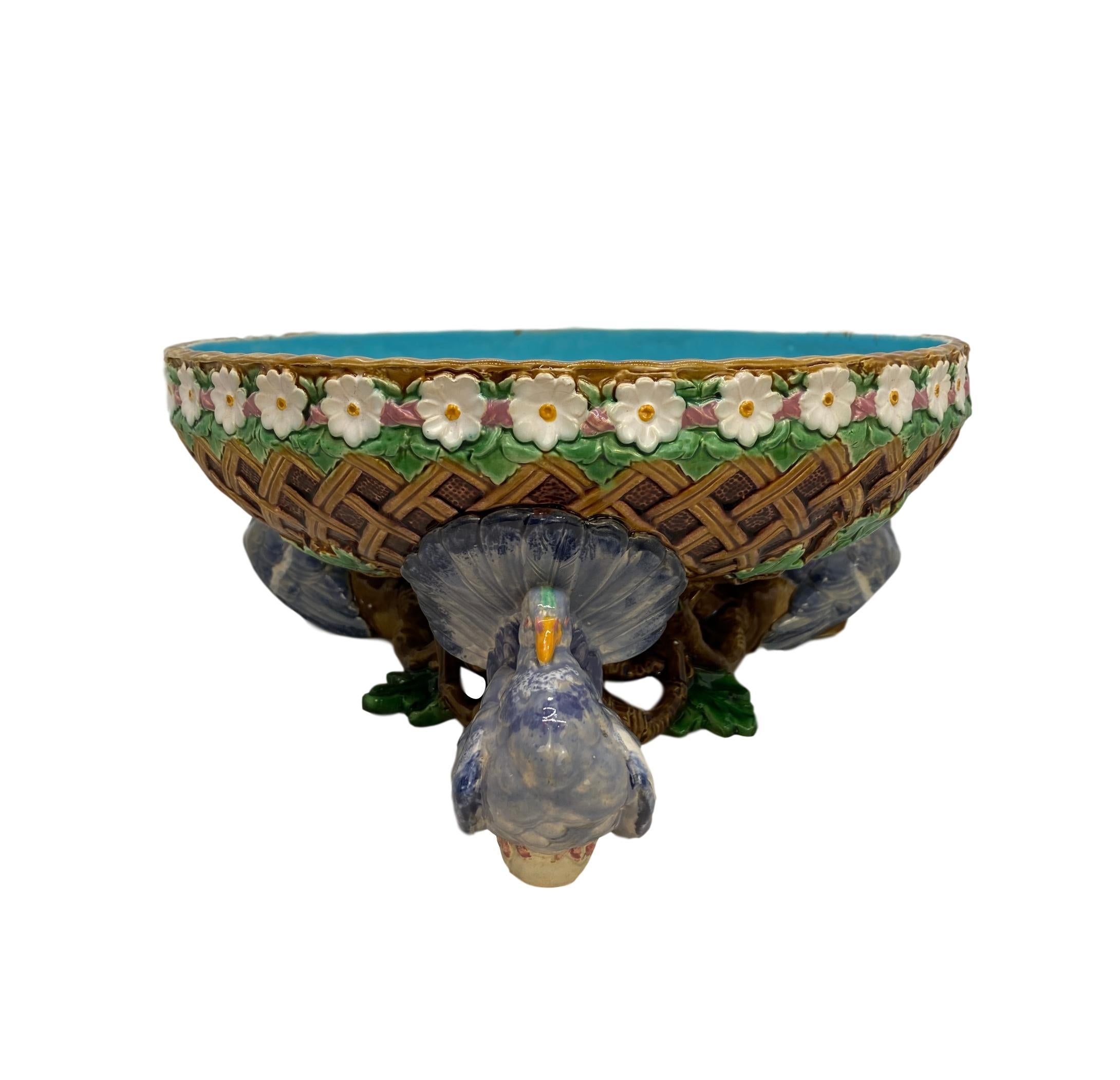 Minton Majolica fruit bowl, 12-ins. Dia., formed as a blind latticework basket with a turquoise interior, with a daisy chain molded rim, supported by three fan-tail pigeons glazed in shades of blue, white, and grey with yellow beaks, on oak branches