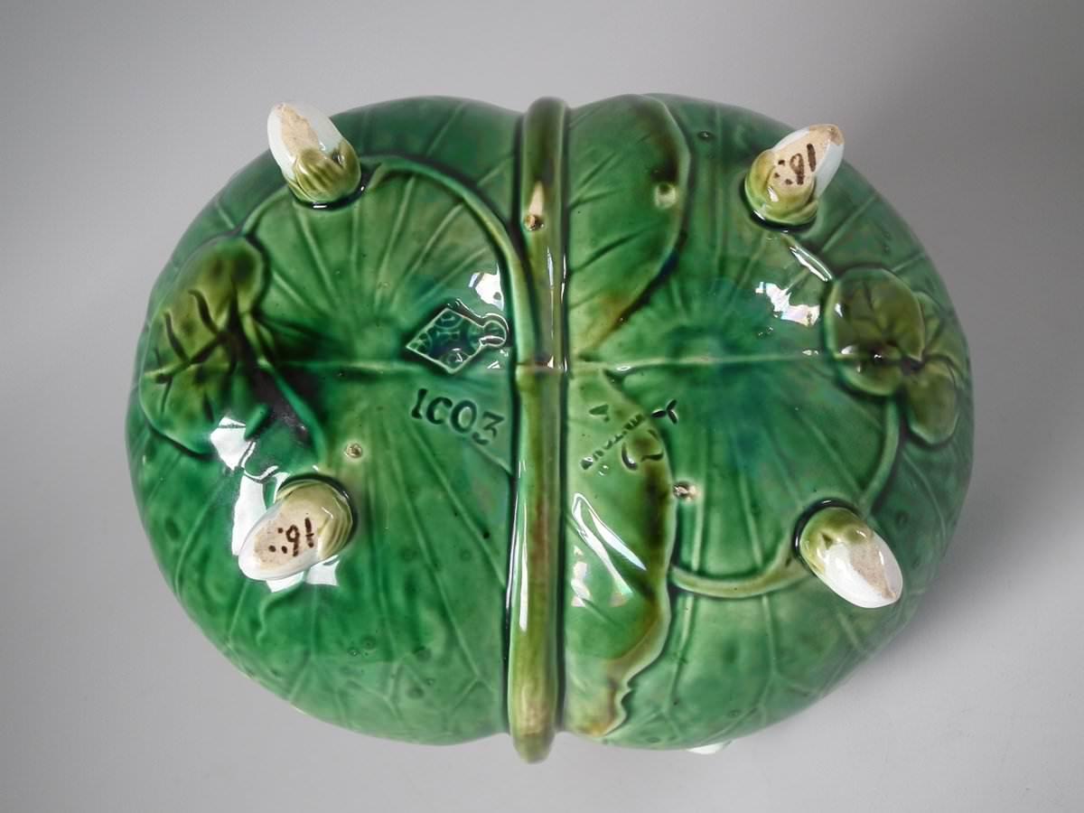 Minton Majolica basket which features pond lily leaves and flowers tied together with lily stems which form the handle. Four flower bud feet. Coloration: green, turquoise, white, are predominant. Bears a pattern number, '1603'. English diamond