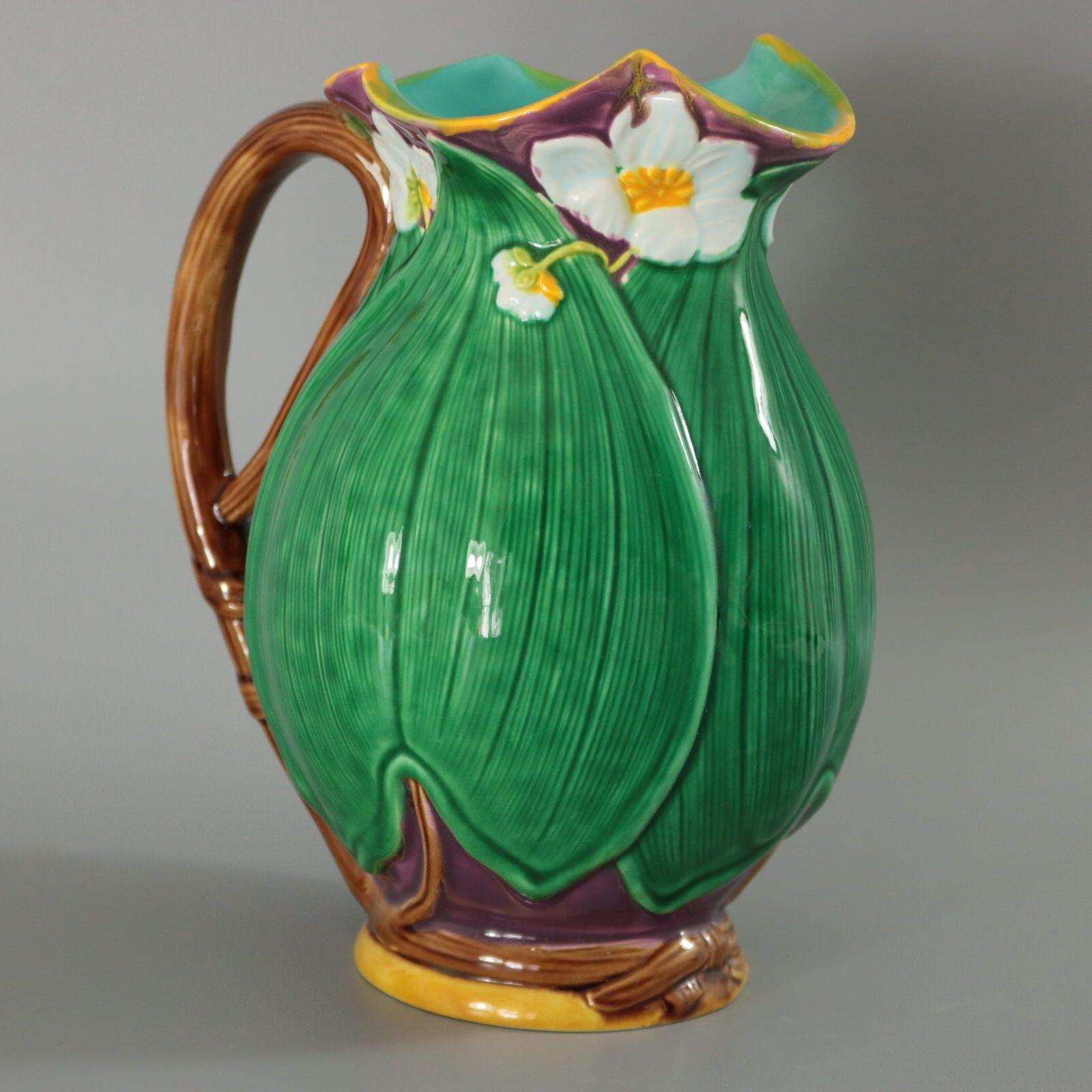 Minton Majolica jug/pitcher which features flowering lilies and lily pads. Colouration: green, dark pink, white, are predominant.