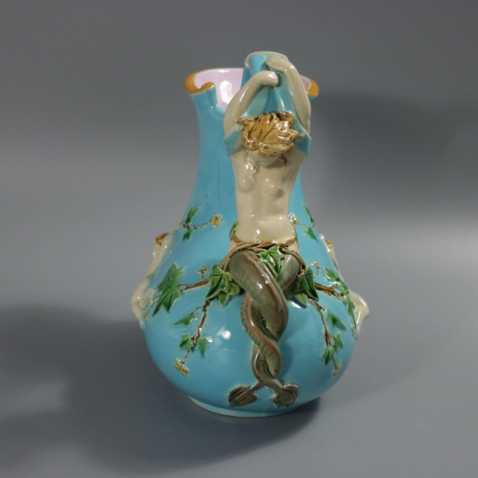 Minton Majolica jug/pitcher which features a handle in the form of a mermaid with entwined tail, a satyr mask below the spout and cherubs hanging from grape vines across the sides. Turquoise ground version. Colouration: turquoise, cream, green, are