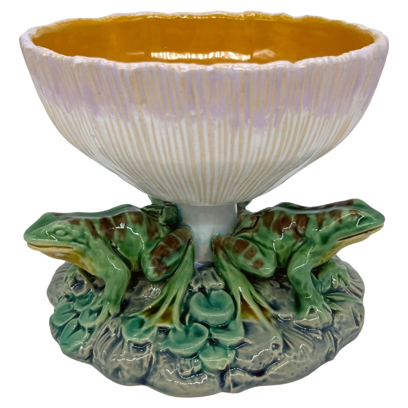 Minton Majolica Taza, molded as an inverted mushroom, the bowl interior glazed in orange, with three naturalistically modeled and glazed frogs around the stem, on a round, plant and rock-work base. Impressed marks to reverse: 'MINTON;' date cypher