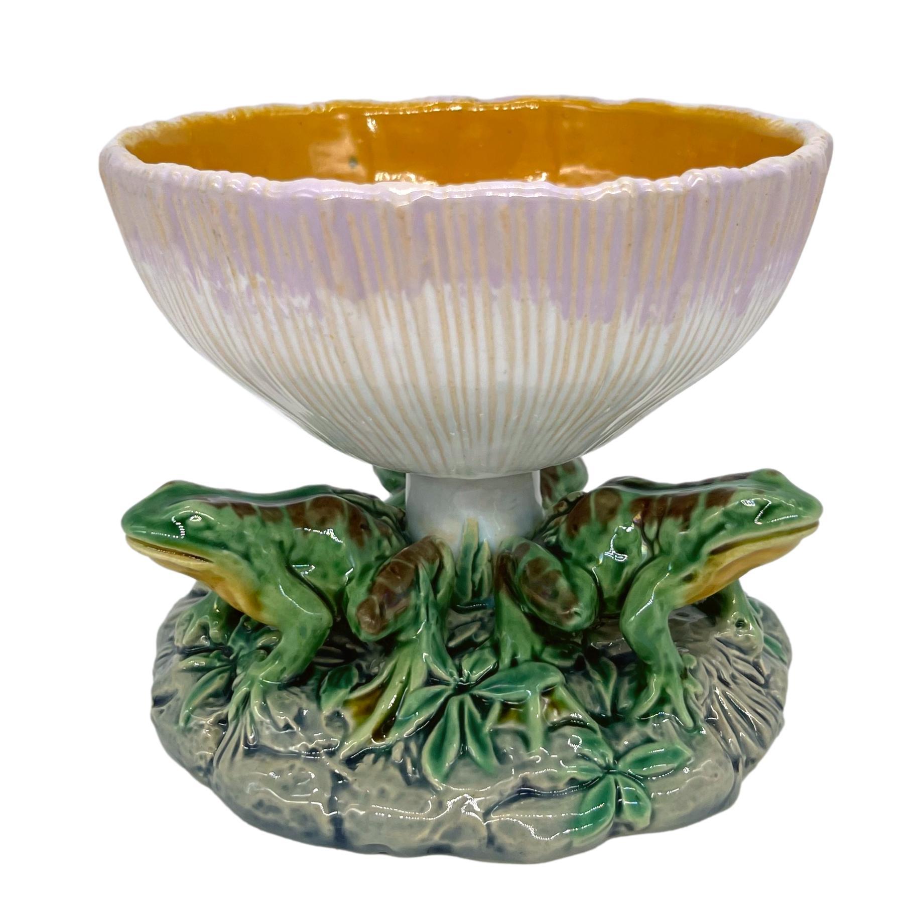 Taza de mayólica Minton, moldeada como una seta invertida, el interior del cuenco esmaltado en naranja, con tres ranas naturalísticamente modeladas y esmaltadas alrededor del tallo, sobre una base redonda, vegetal y de rocalla. Marcas impresas en el