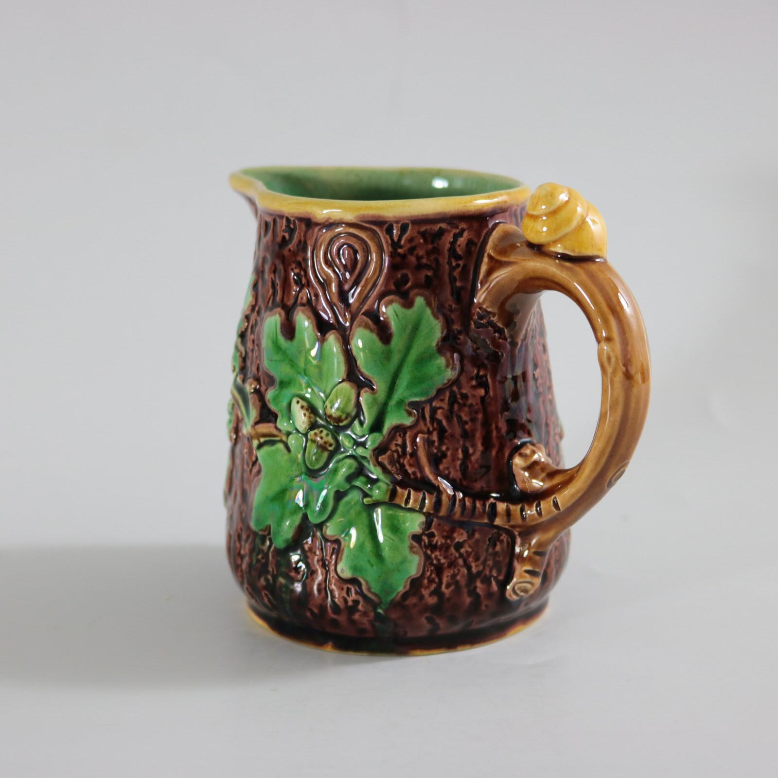 Minton Majolica jug/pitcher which features oak leaves and acorns to the sides and a snail to the handle. Colouration: brown, green, yellow, are predominant. The piece bears maker's marks for the Minton pottery.