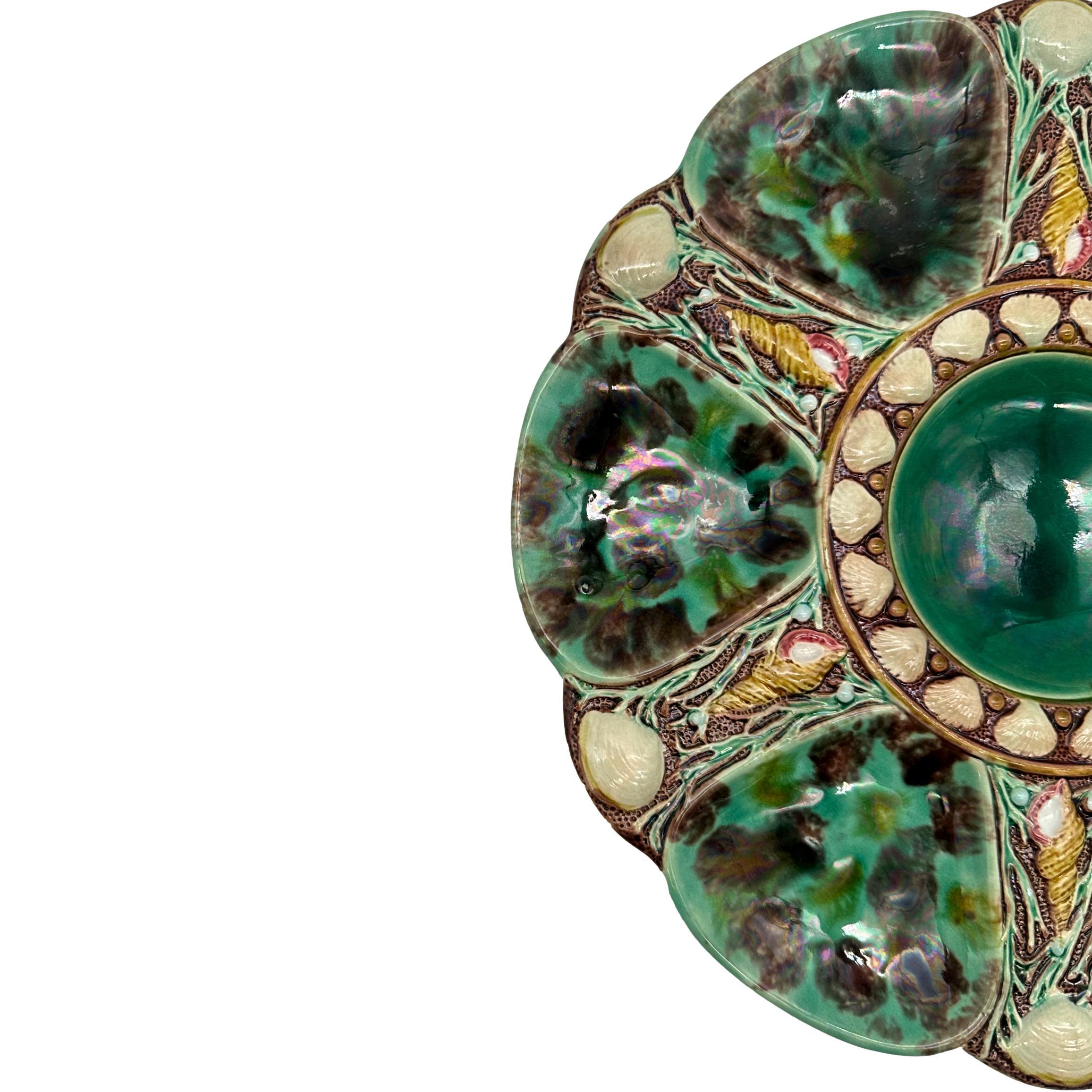 Minton Majolica Oyster Plate, the relief-molded dish with six wells glazed in green and brown mottled leopard spots, each well separated by shells and seaweed, the center well glazed in green and banded with shells, the reverse with impressed and