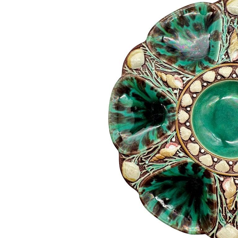 Minton Majolica Oyster Plate, the relief-molded dish with six wells glazed in mottled leopard spots of green and dark brown, each well separated by shells and seaweed, the center well glazed in green and banded with shells, the reverse with