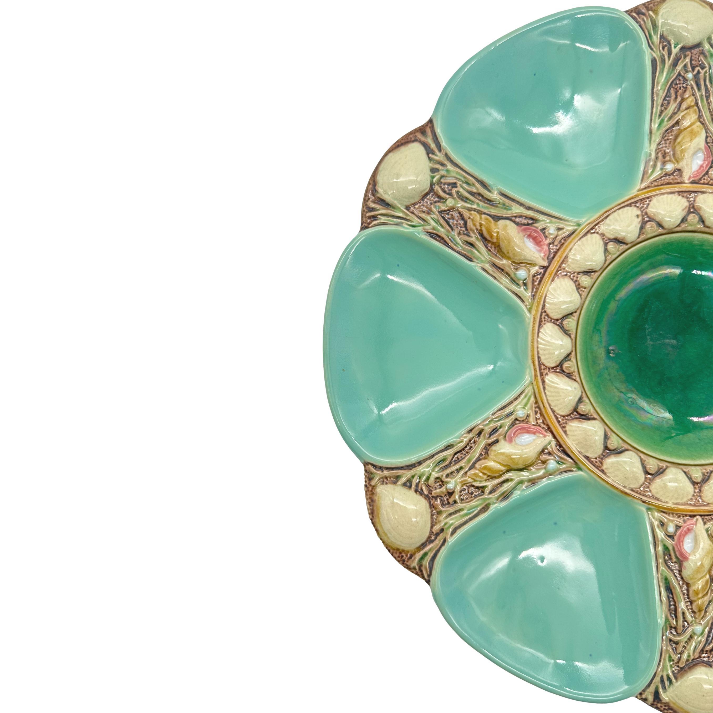 Minton Majolica Oyster Plate, the relief-molded dish with six oyster wells glazed in seafoam green, each well separated by shells and seaweed and a naturalistically molded and glazed auger shell, the center well glazed in green and banded with