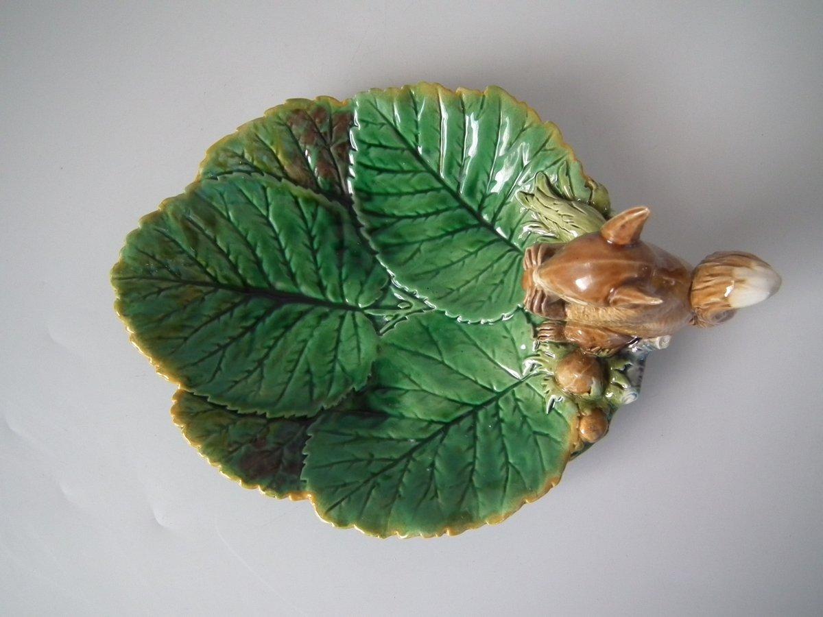Minton Majolica nut dish which features a squirrel holding a nut. Coloration: green, brown, ochre, are predominant. The piece bears maker's marks for the Minton pottery. Bears a pattern number, '1522'. English diamond registration mark for the date