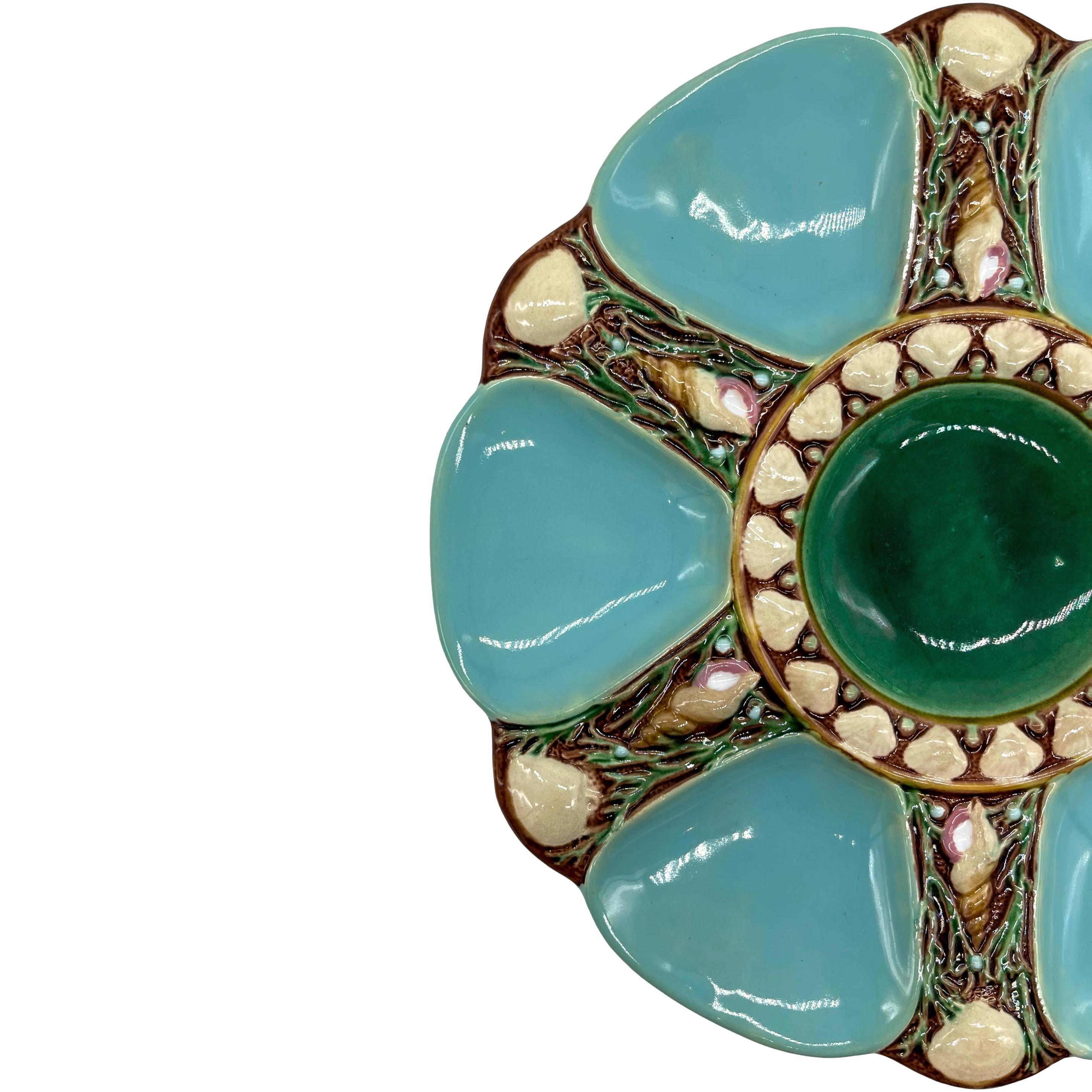 Minton Majolica Oyster Plate, the relief-molded dish with six oyster wells glazed in turquoise, each well separated by shells and seaweed and a naturalistically molded and glazed auger shell, the center well glazed in green and banded with shells,