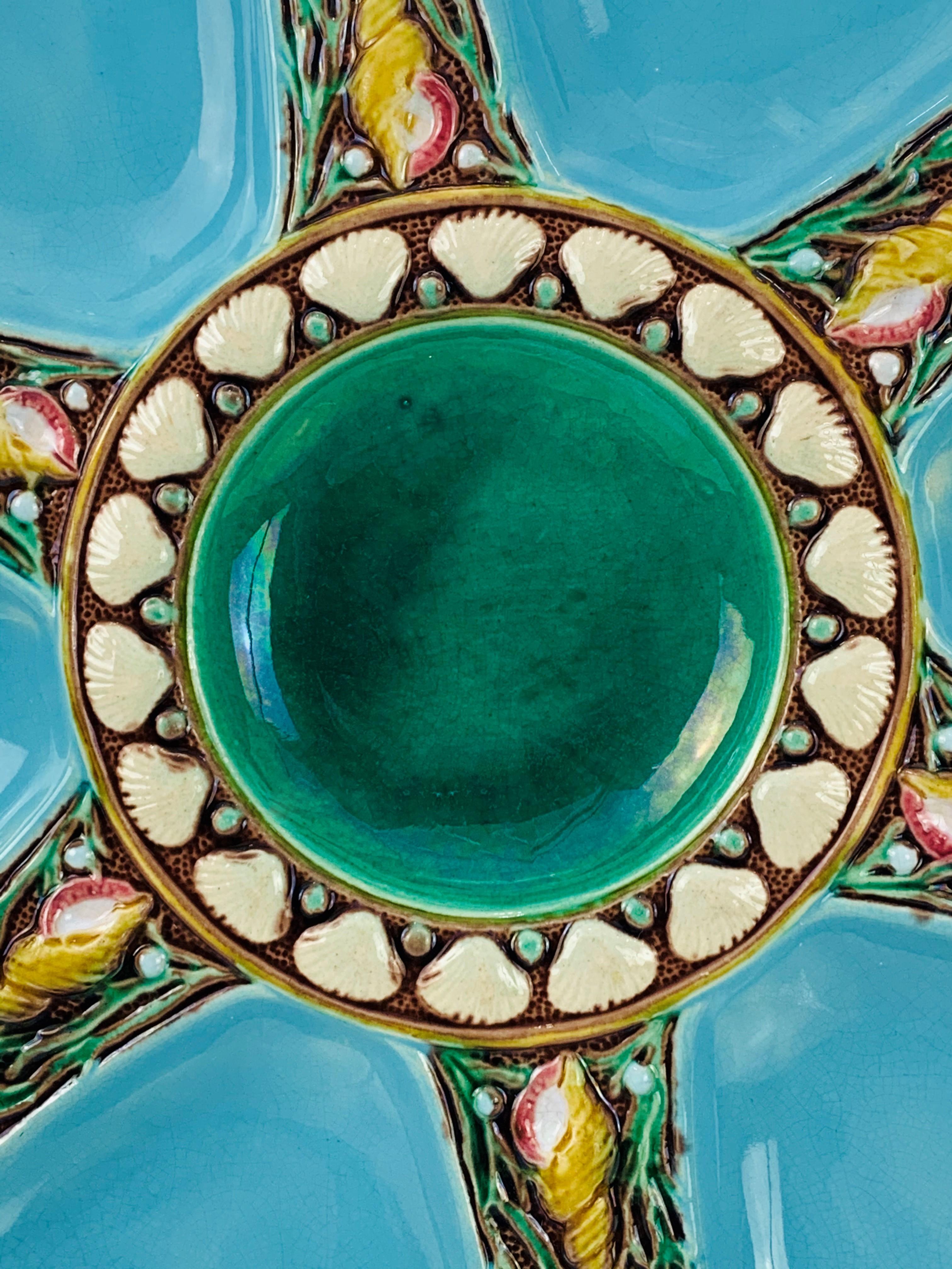 Minton Majolica six well oyster plate, the wells glazed in turquoise blue, each well separated by shells and seaweed, the central well glazed in green, bordered with shells. Impressed marks to reverse: 'Minton' with Minton date cypher for 1873