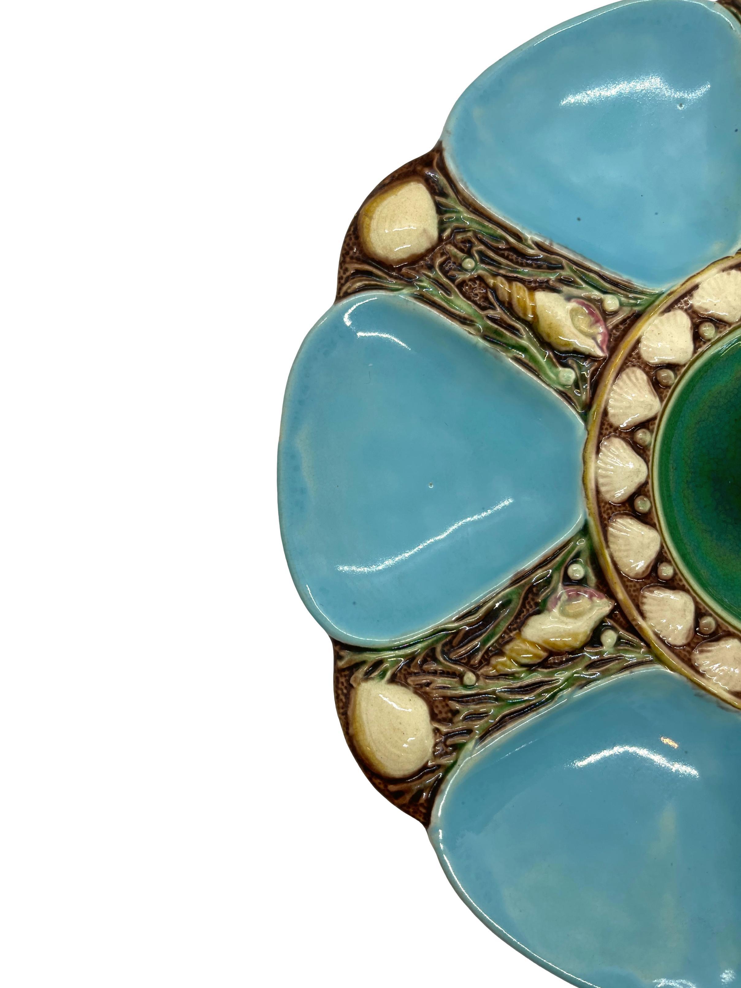 Minton Majolica six-well oyster plate, the wells glazed in turquoise blue, each well separated by shells and seaweed, the central well glazed in green, bordered with shells. Impressed marks to reverse: 'MINTONS' with Minton date cypher for 1874,