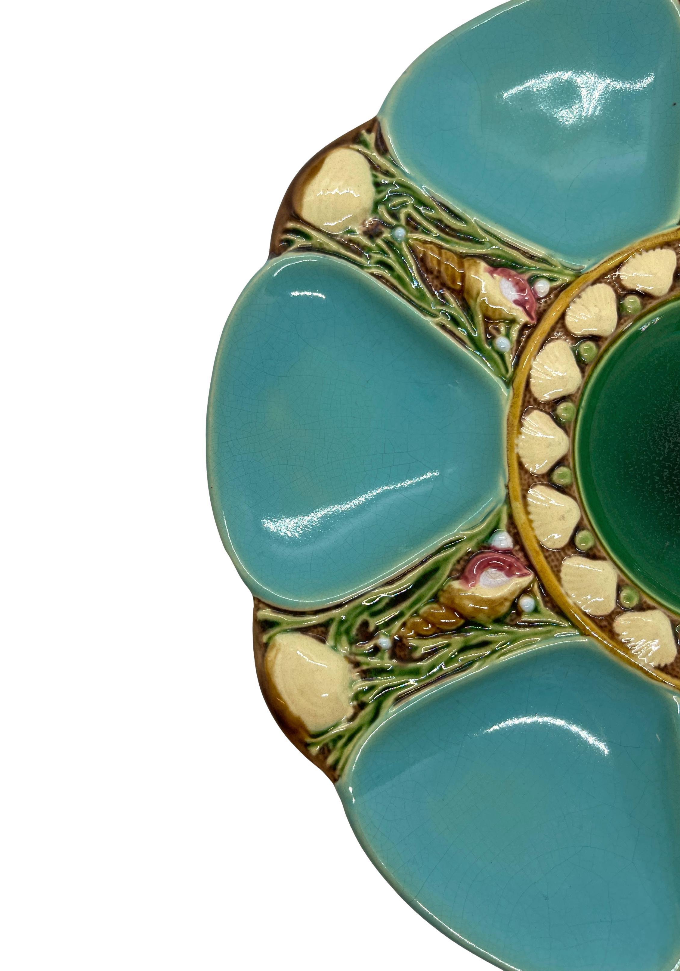 Minton Majolica six-well oyster plate, the wells glazed in turquoise blue, each well separated by shells and seaweed, the central well glazed in green, bordered with shells. Impressed marks to reverse: 'MINTONS' with Minton date cypher for 1895