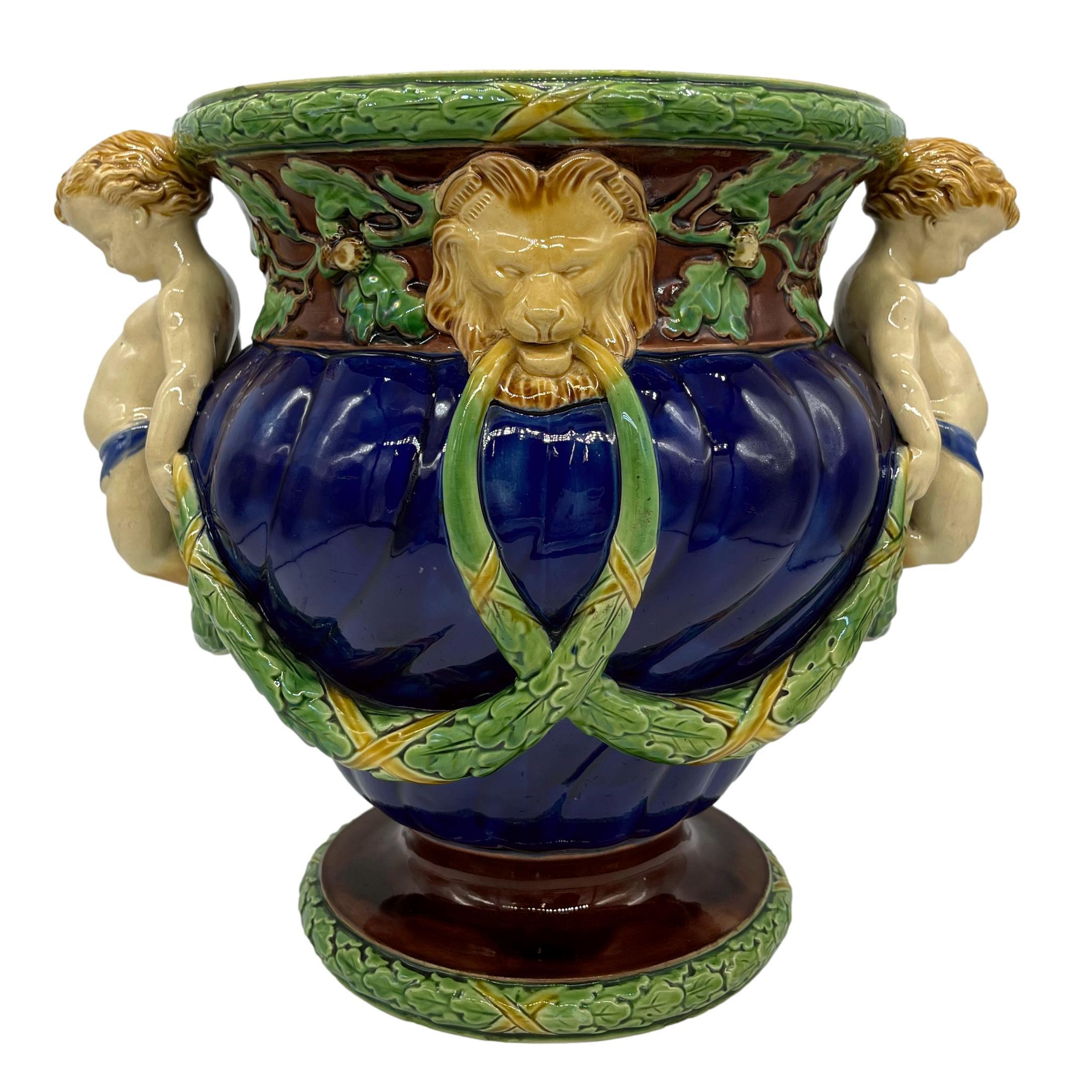 Minton Majolica wine cooler, the spiral-lobed body glazed in cobalt blue, with applied oak leaf garlands and two fauns forming the handles, the neck banded with naturalistic oak branches, leaves, and acorns, with lion mask central medallions, the