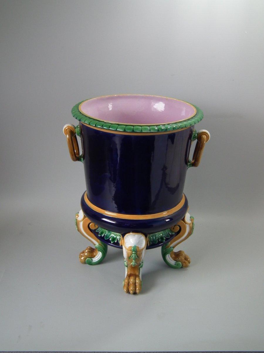 Minton Majolica wine cooler which features ring handles and lion paw feet. Coloration: cobalt blue, ochre, green, are predominant. The piece bears maker's marks for the Minton pottery. Bears a pattern number, '1083'. Marks include a factory specific