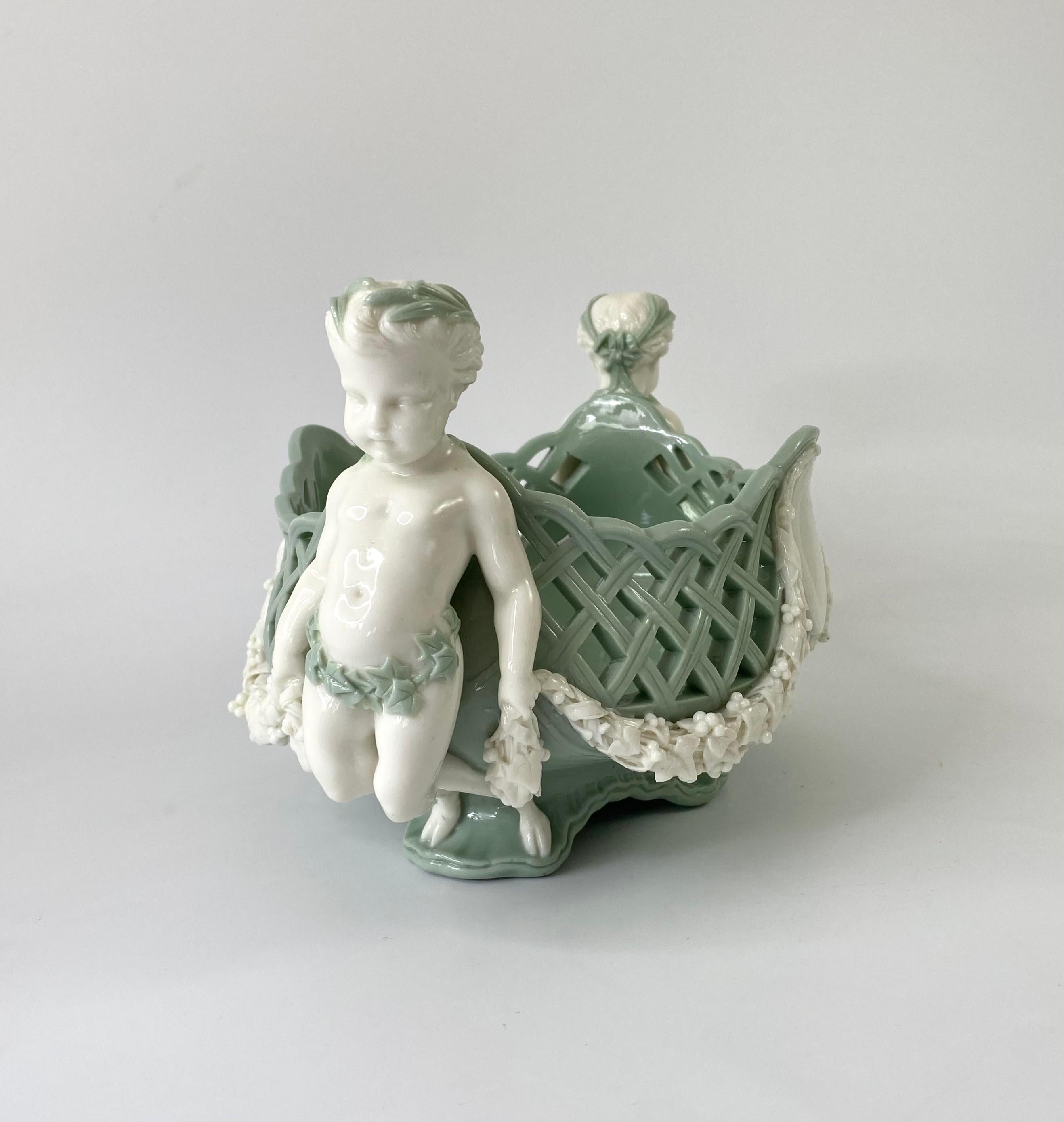A fine Minton pate sur pate porcelain basket, dated 1867. The celadon green ground lattice worked basket, supported by two Bacchanalian cherubs, and set upon scroll feet. The cherubs hold between them, a graping vine swag, suspended over twin oval