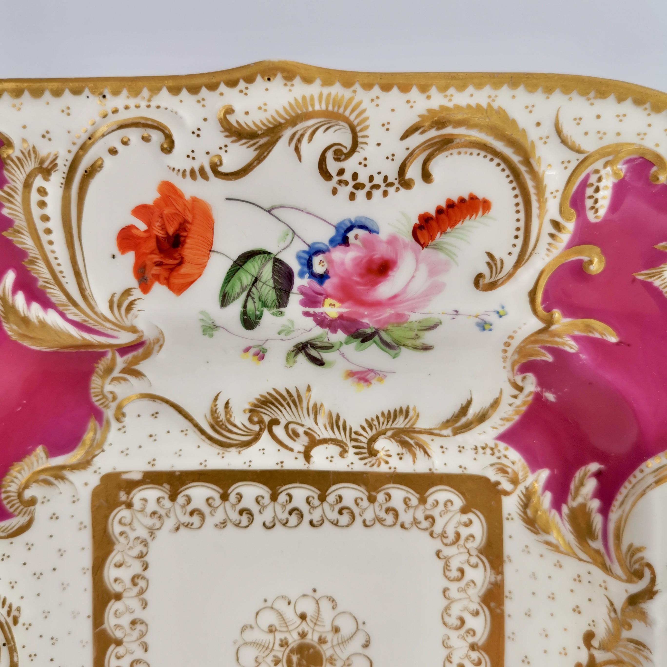 This is a rather stunning cake plate made by Minton in about 1830, which was the Rococo Revival era. This plate is decorated in a maroon ground with hand painted flower reserves and lavish gilding, and would have belonged to a large tea service.
