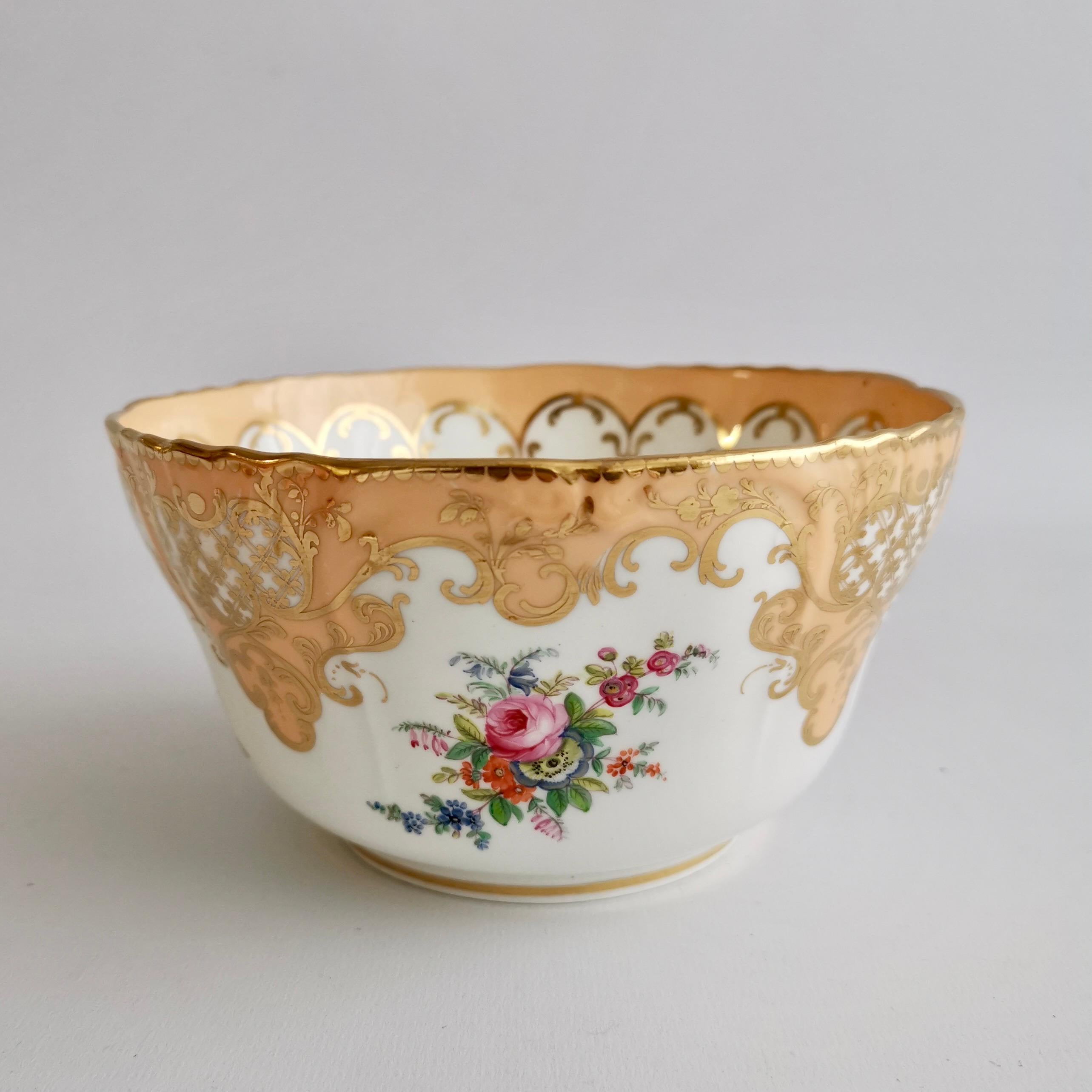 This is a beautiful slop bowl made around 1845 by Minton. It is decorated with a beautiful apricot orange ground and rich gilding, and four finely printed and then hand-colored flower arrangements. The bowl is shaped in a beautiful diapered