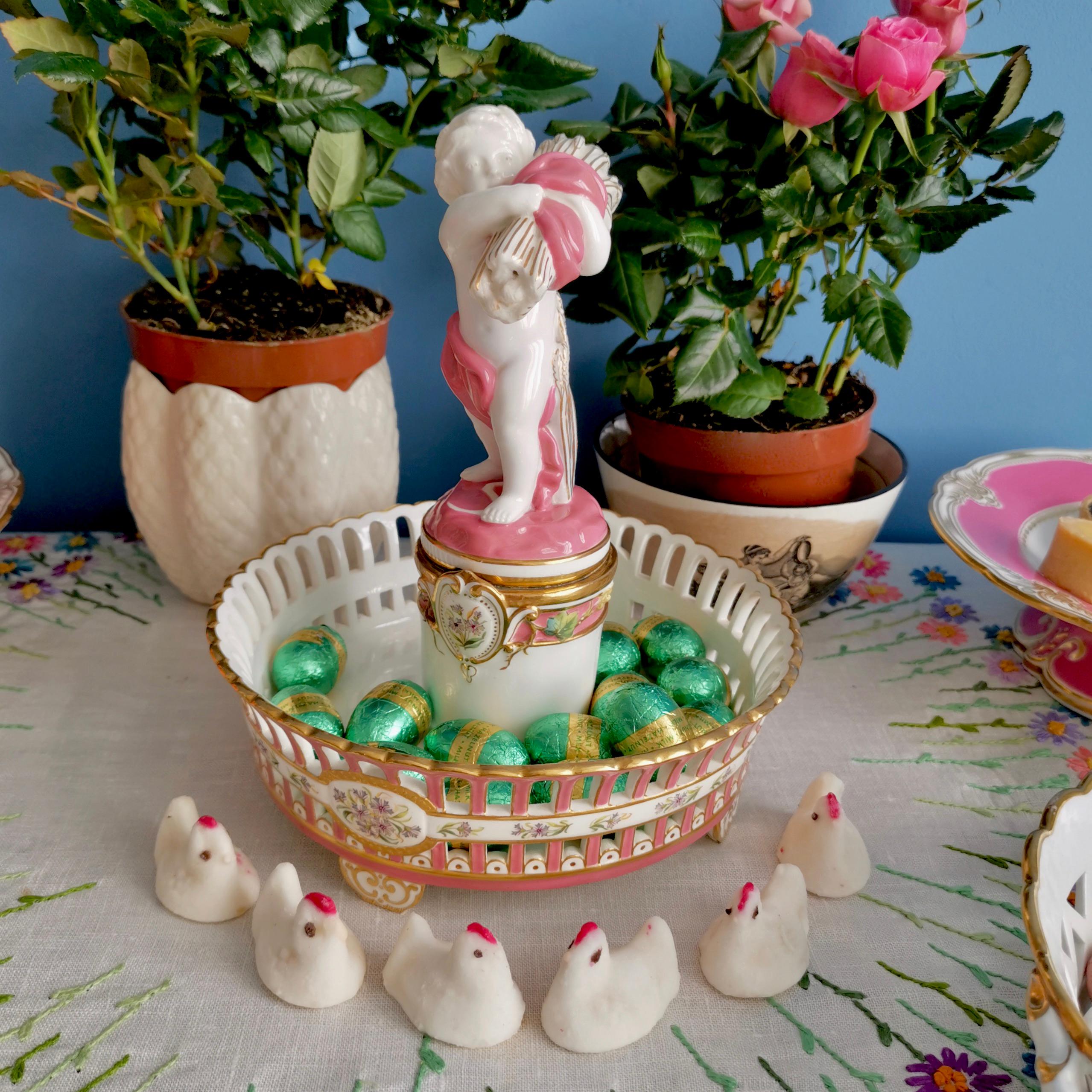 This is a beautiful centre piece tazza made by Minton in 1891, which was the Victorian era. The piece is made in white and pink porcelain and the centre consists of a cherub carrying a sheaf of wheat. This tazza would make a fabulous display on your