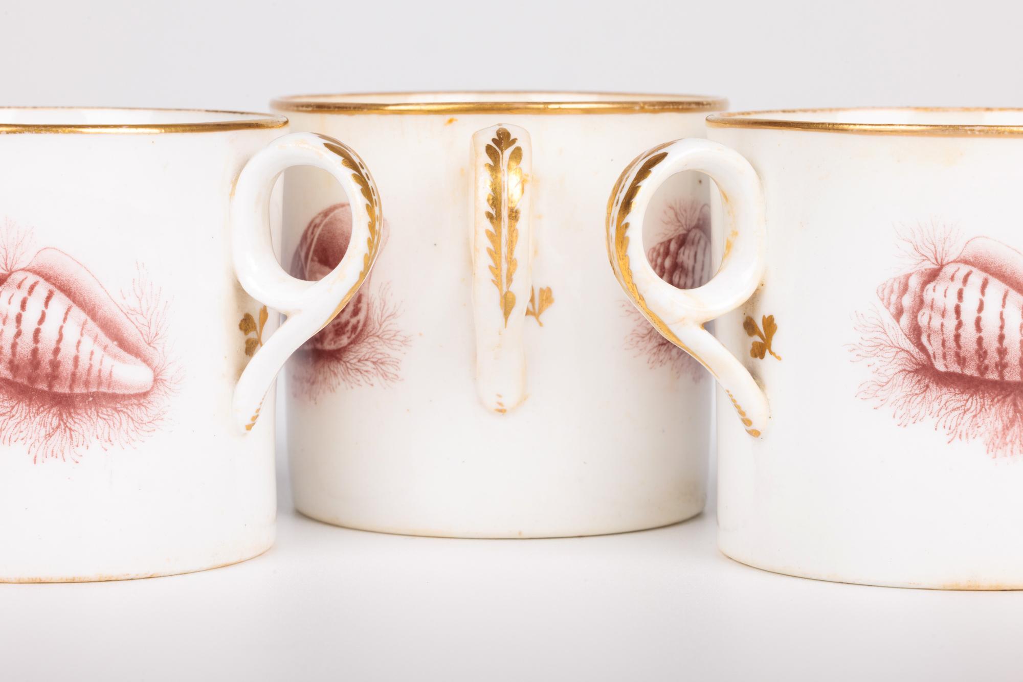 A rare set of three Georgian antique porcelain coffee cups printed with shells by renowned makers Minton and dating from around 1800. The coffee cans are of cylindrical shape with loop handles applied to the sides and are printed with puce shell