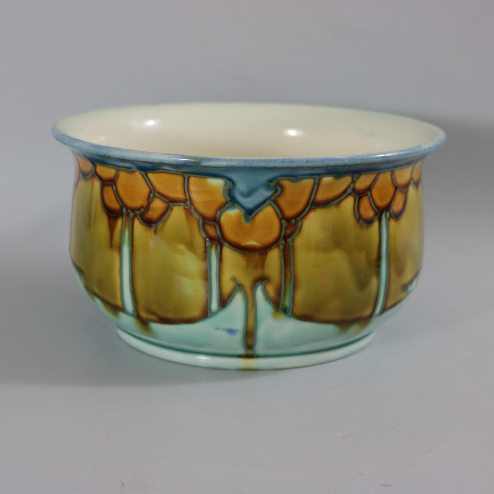 Minton Secessionist No.8 chamber pot decorated with Art Nouveau style tree motifs. Glazed in blue, ochre and green with gray tube lining. Cream interior and underside. Three stilt marks to underside along with maker's marks printed 'MINTONS LTD