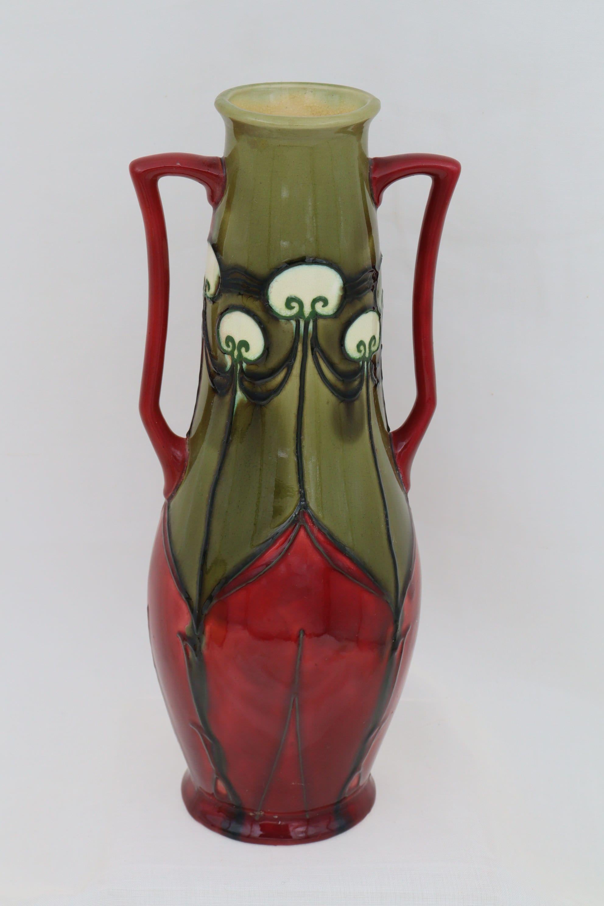 This Minton vase is from their Secessionist ware range and is decorated with the pattern number 10. The pattern is outlined by tube lining then filled with majolica glazes, in this case red, olive green and white. The shape number is 3747 which is a