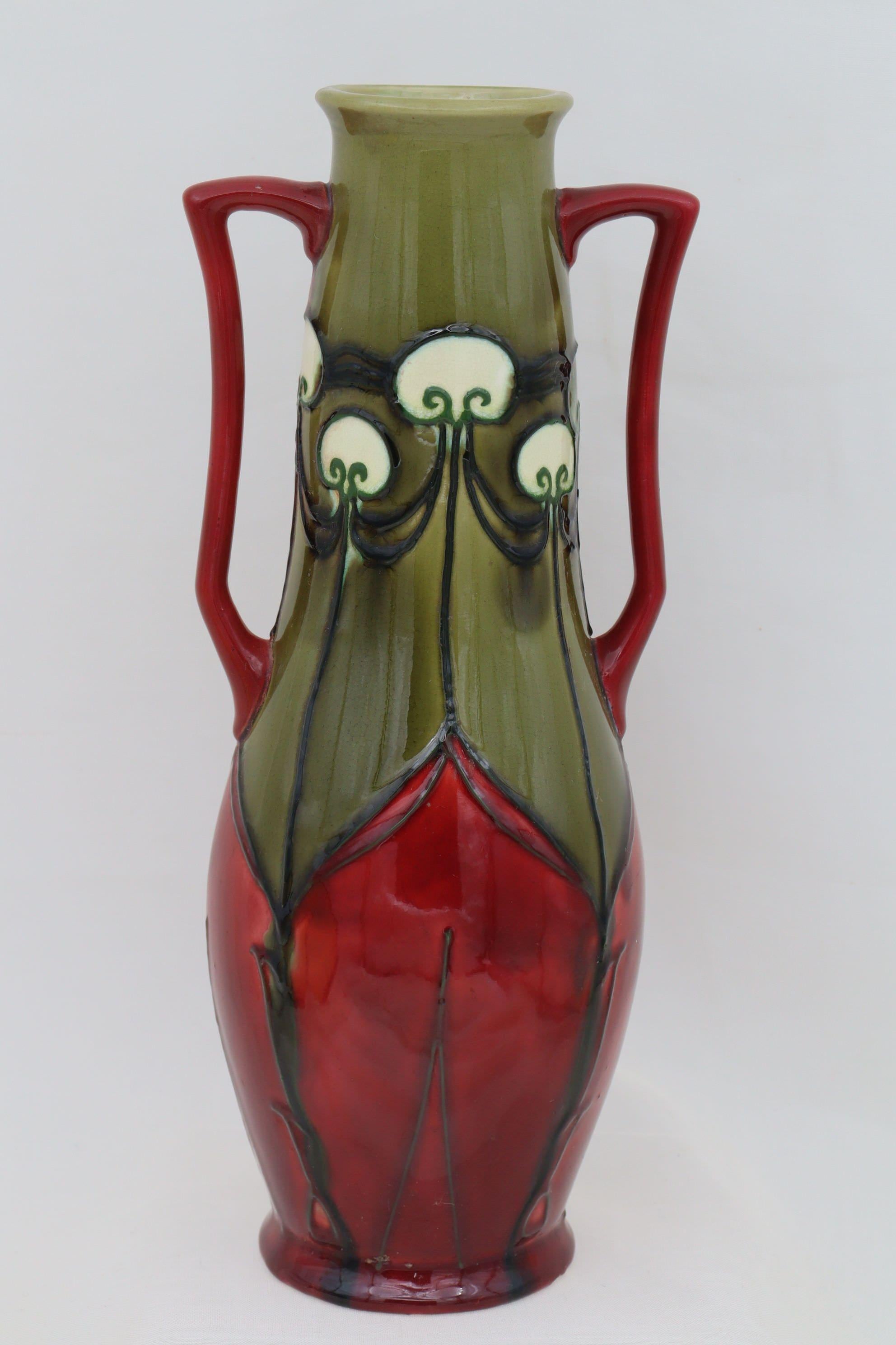 This Minton vase is from their Secessionist ware range and is decorated with the pattern number 10. The pattern is outlined by tube lining then filled with majolica glazes, in this case red, olive green and white. The shape number is 3747 which is a