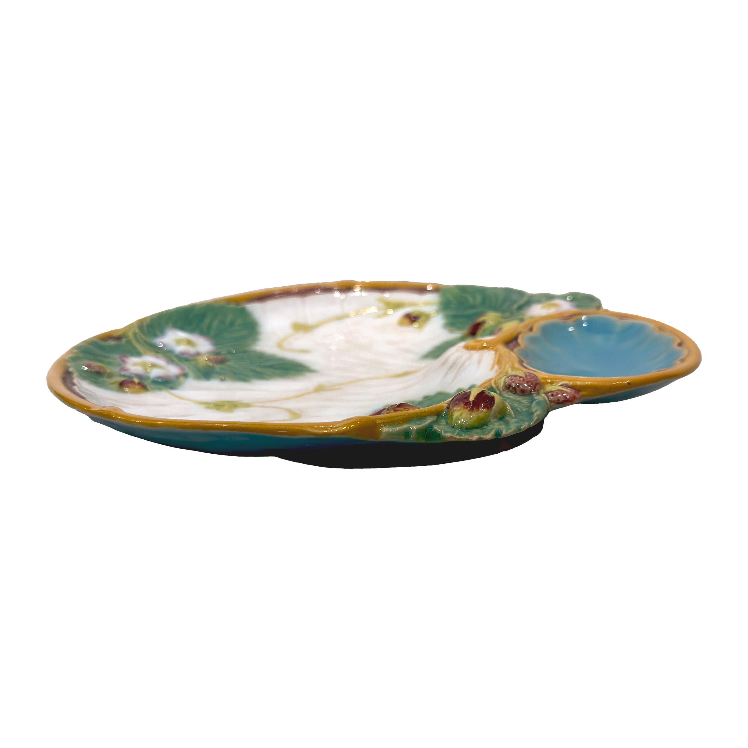 Cette magnifique assiette en faïence anglaise de Minton est un véritable chef-d'œuvre du XIXe siècle, fabriqué en 1878. Orné d'un charmant motif en terre cuite, il représente des fraises rouges dodues nichées parmi des feuilles de fraisier fleuries.