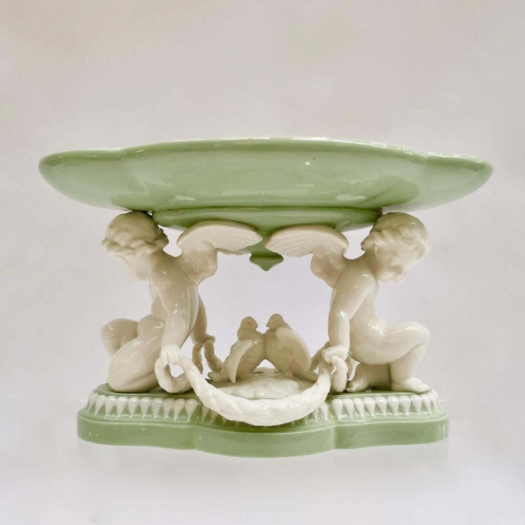 This is a beautiful porcelain tazza or comport made by Minton in 1855, which was the Victorian era. It is made of parian porcelain and has a white and celadon green color with cherubs and loving doves.

Minton was one of the pioneers of English