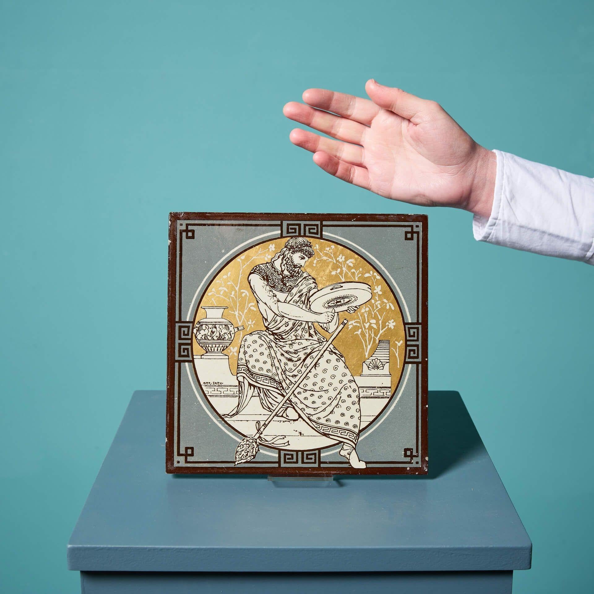 An antique Minton tile from the series ‘Classical Figures with Musical Instruments’ designed by the artist John Moyr Smith.

This 8 inch tile depicts a nobleman in roman style dress playing a tambourine in a neoclassical scene, hand painted on a