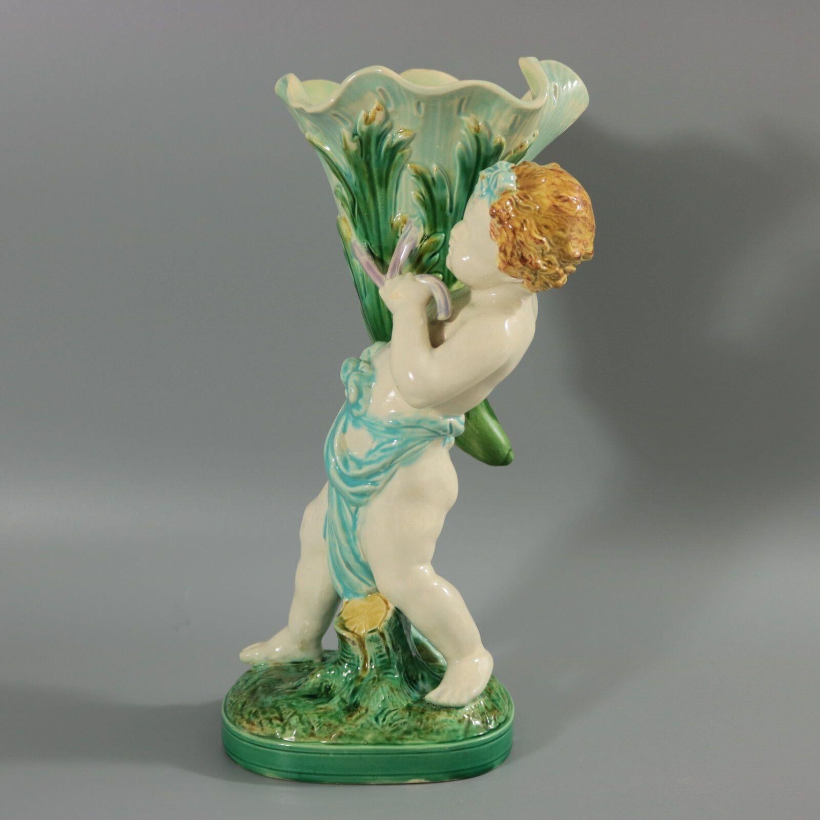 Minton Majolica flower holder which features a putti wearing drapes, carrying a cornucopia vase. Colouration: green, turquoise, white, are predominant. The piece bears maker's marks for the Minton pottery. Bears a pattern number, '3118'. Marks
