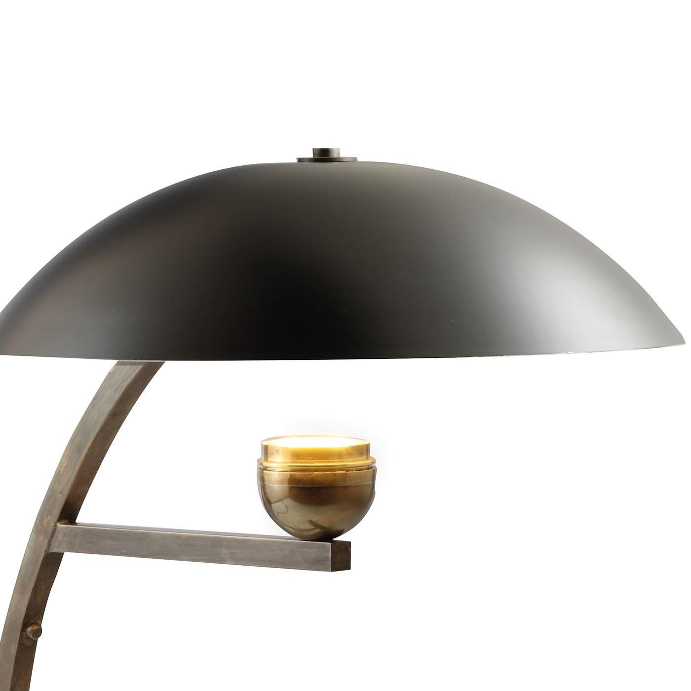This striking lamp features a unique series of curved and straight elements in brass with a bronze finish that make up its structure. A short shelf in the center supports the light that shines upwards, shielded by the semi-spherical metal shade