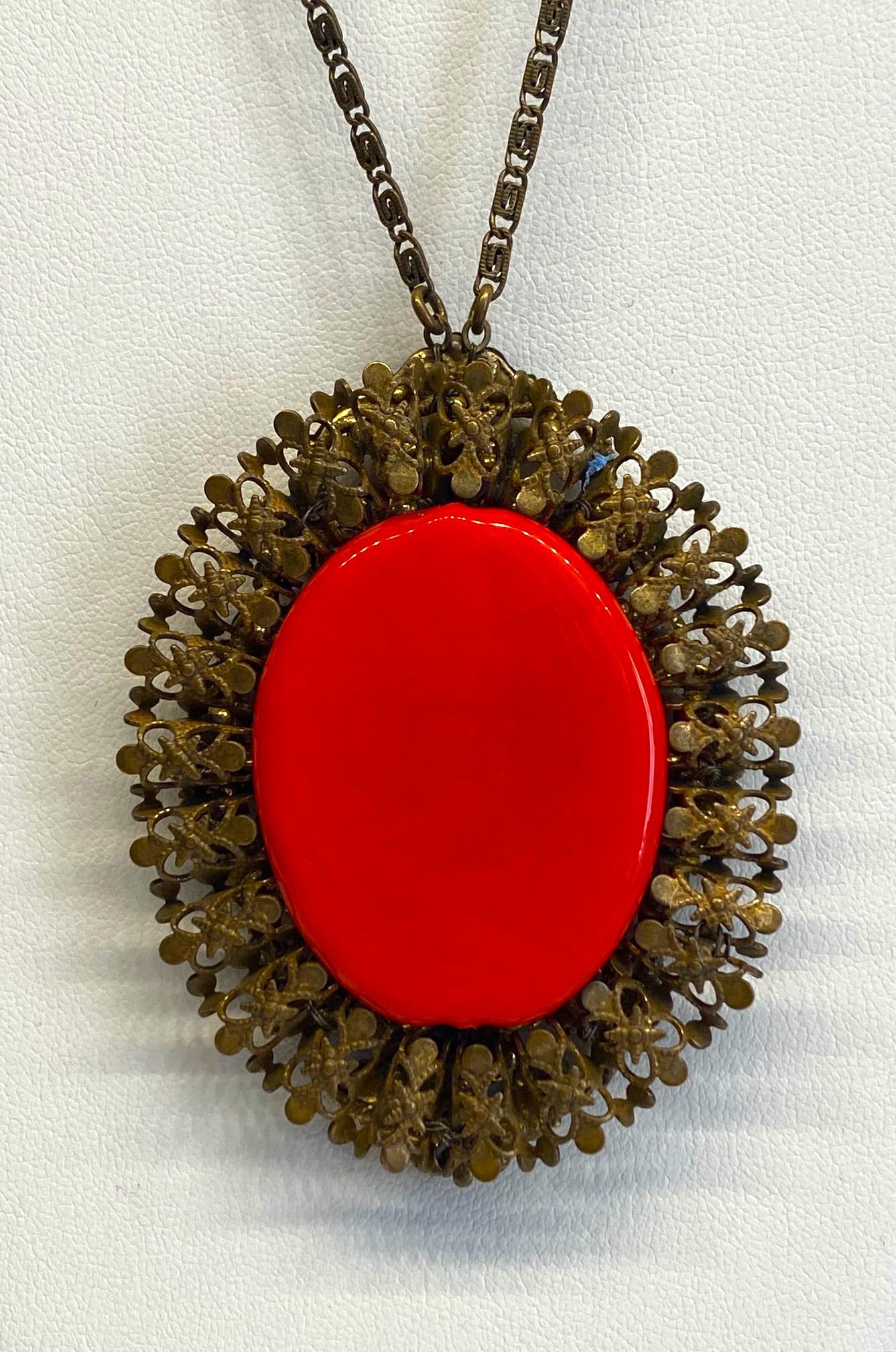 A vintage Miriam Haskell 1960s pendant necklace with opaque orange red glass center. The finish is Haskell's well known antique Russian gold plate. The pendant is 2.13 inches wide, 2.75 inches high and .38 of an inch deep. The center is a hand