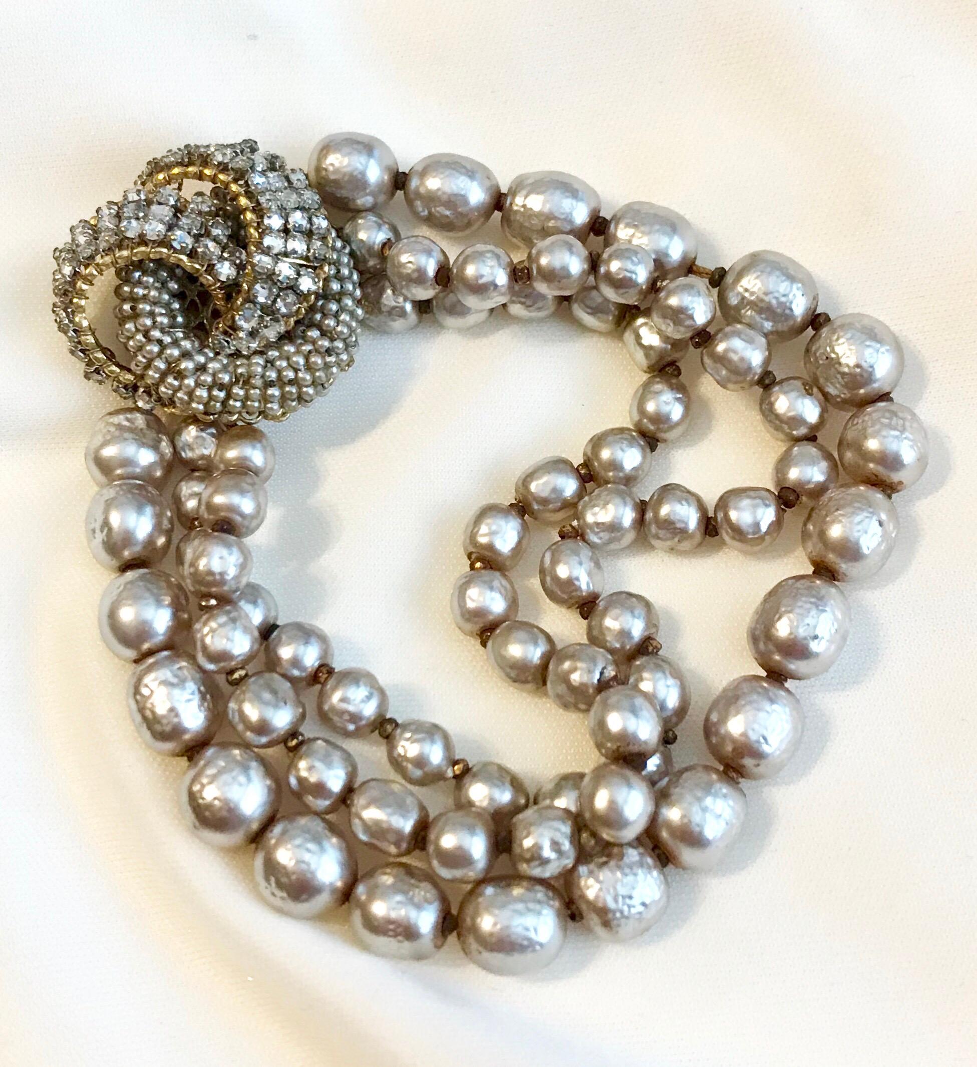 Circa 1950s Miriam Haskell triple strand, soft-white baroque faux-pearl bracelet with an ornate jeweled clasp.  The clasp is covered with prong set rhinestones and faux-seed pearls and marked on the back, Miriam Haskell.  This piece is from the