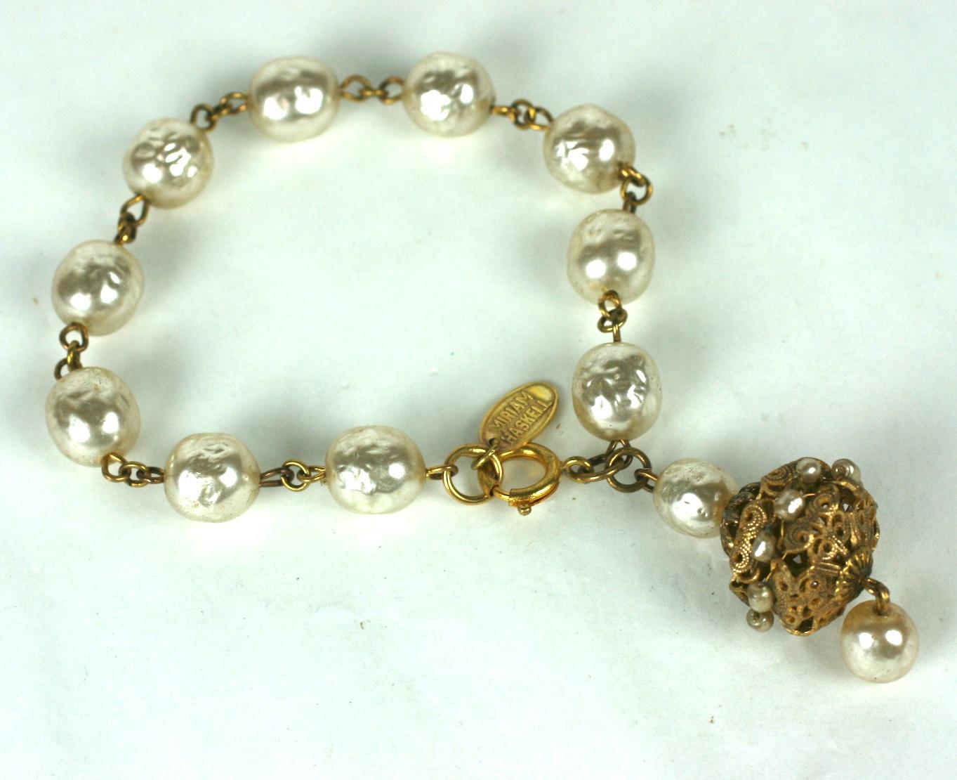 Miriam Haskell faux baroque pearl and gilt fob bracelet. Composed of signature faux baroque pearl links with a large pierced Russian gilt filigree and baroque pearl charm. The dangling  filigree shape fob is decorated with hand sewn round micro