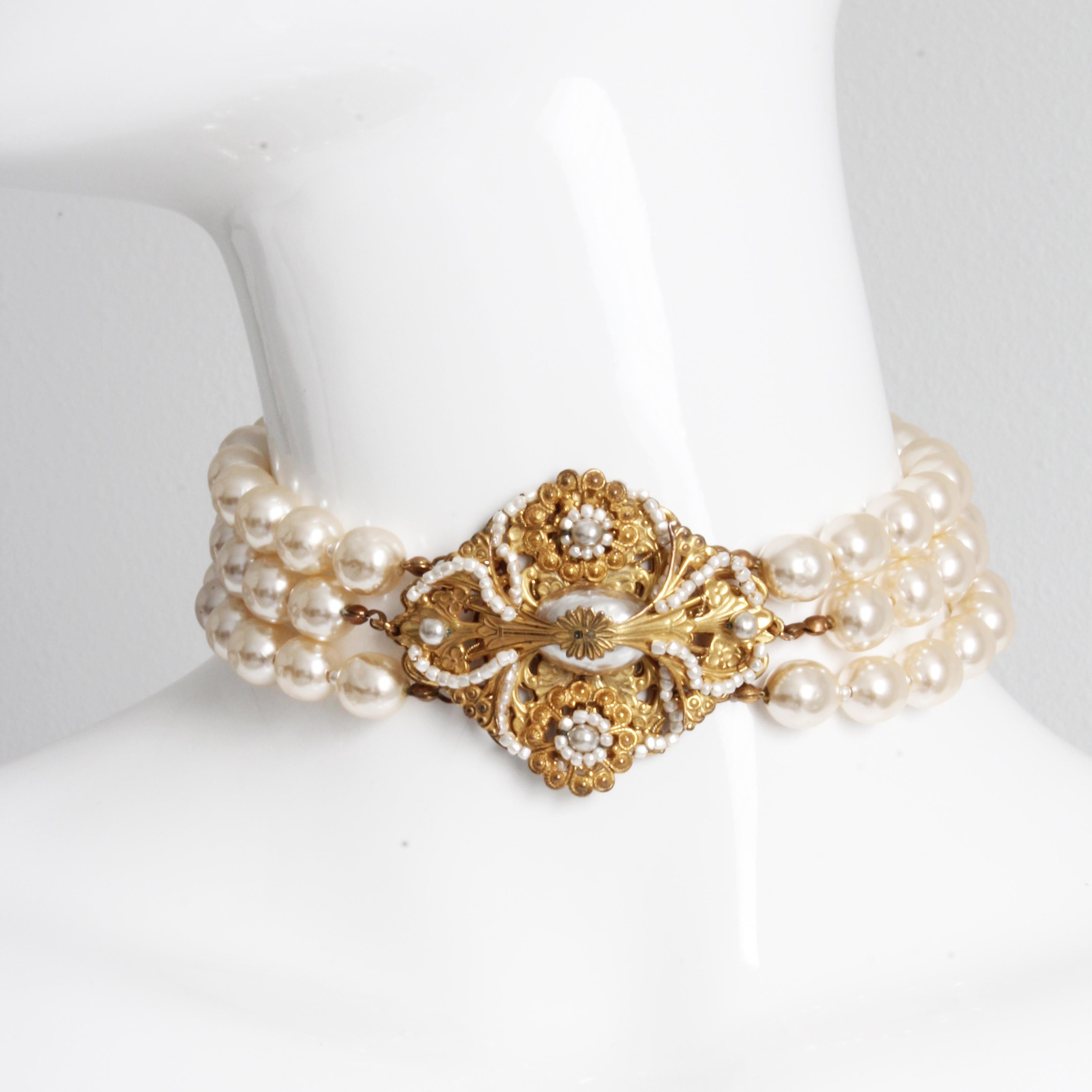 Authentic, preowned, vintage Miriam Haskell Triple Strand Baroque Choker Necklace, likely made in the 1970s.  Features triple strand glass pearls and gold metal floral filigree pendant adorned with tiny pearl seed beads.  Unusual style; fastens with