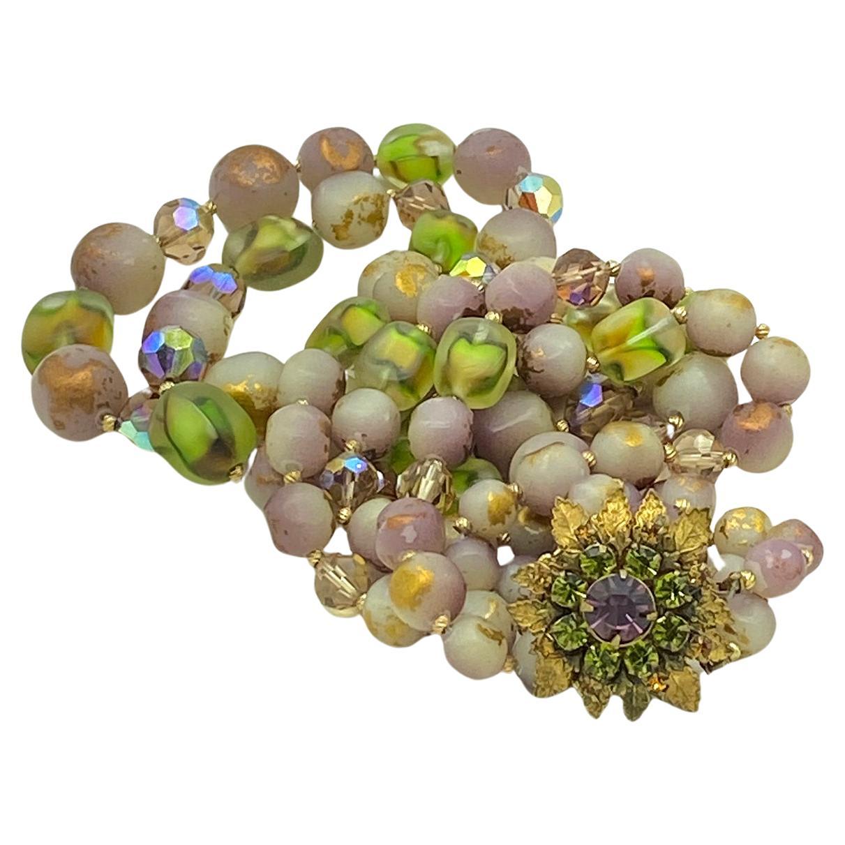 This is a Miriam Haskell double strand necklace and clip-on earrings set. They boast purple, green, gold, all the Marde Gras colors. This hand made set is hi-lighted with a rhinetone with gilded metal leaves box clasp and signed on its back. It