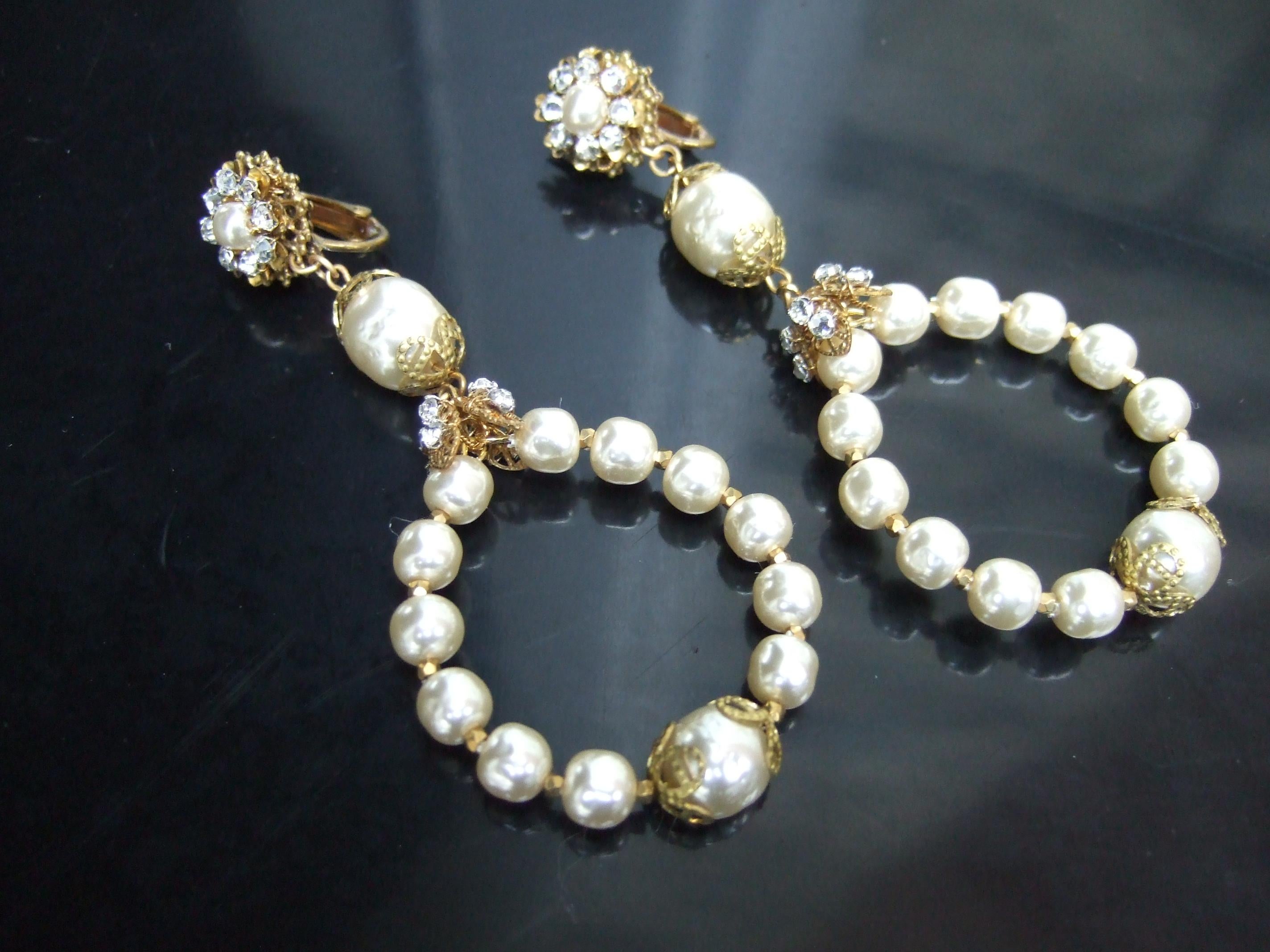 Miriam Haskell Dramatische Glas-Emaille Perle baumeln Reifen Clip-on Ohrringe c 1960s
Die eleganten Ohrringe bestehen aus einem runden, ovalen Ring, der mit einem Band aus Haskells charakteristischen Glasemail-Perlen verziert ist

Der obere Teil ist