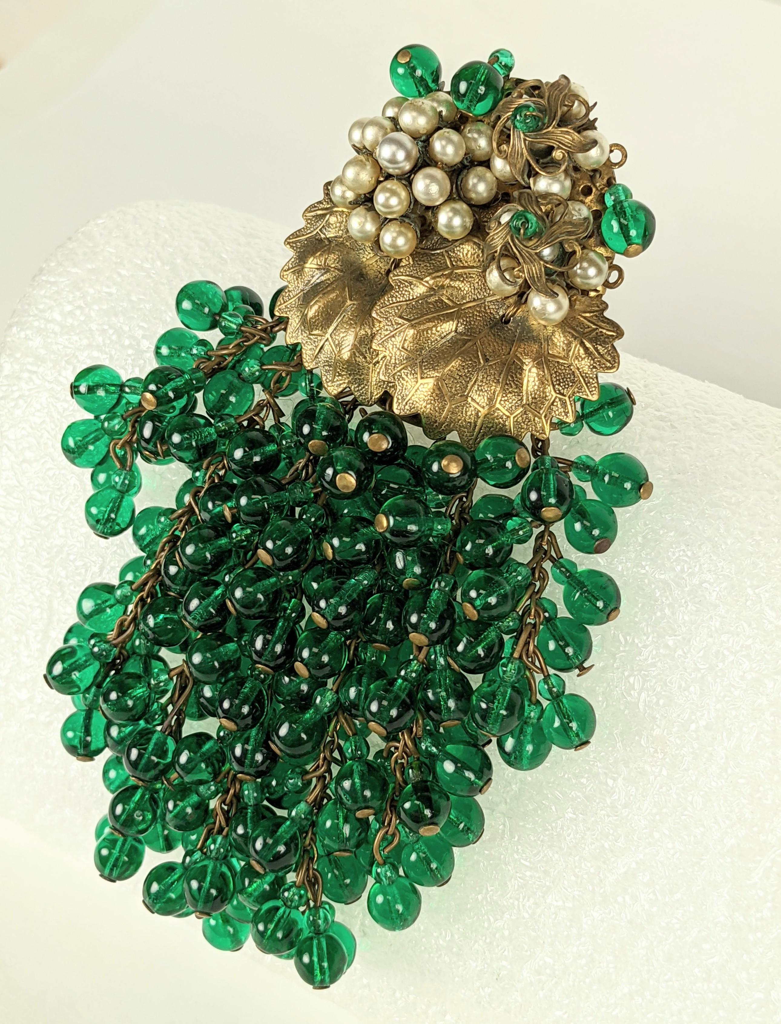 Super large Miriam Haskell Early Green Cluster Bead Clip/Brooch from the 1930's. Clusters of green grape beads fall from brass leaves embroidered with faux pearls and more green beads. 
Early pieces are unsigned as is this one. Clip back fitting for