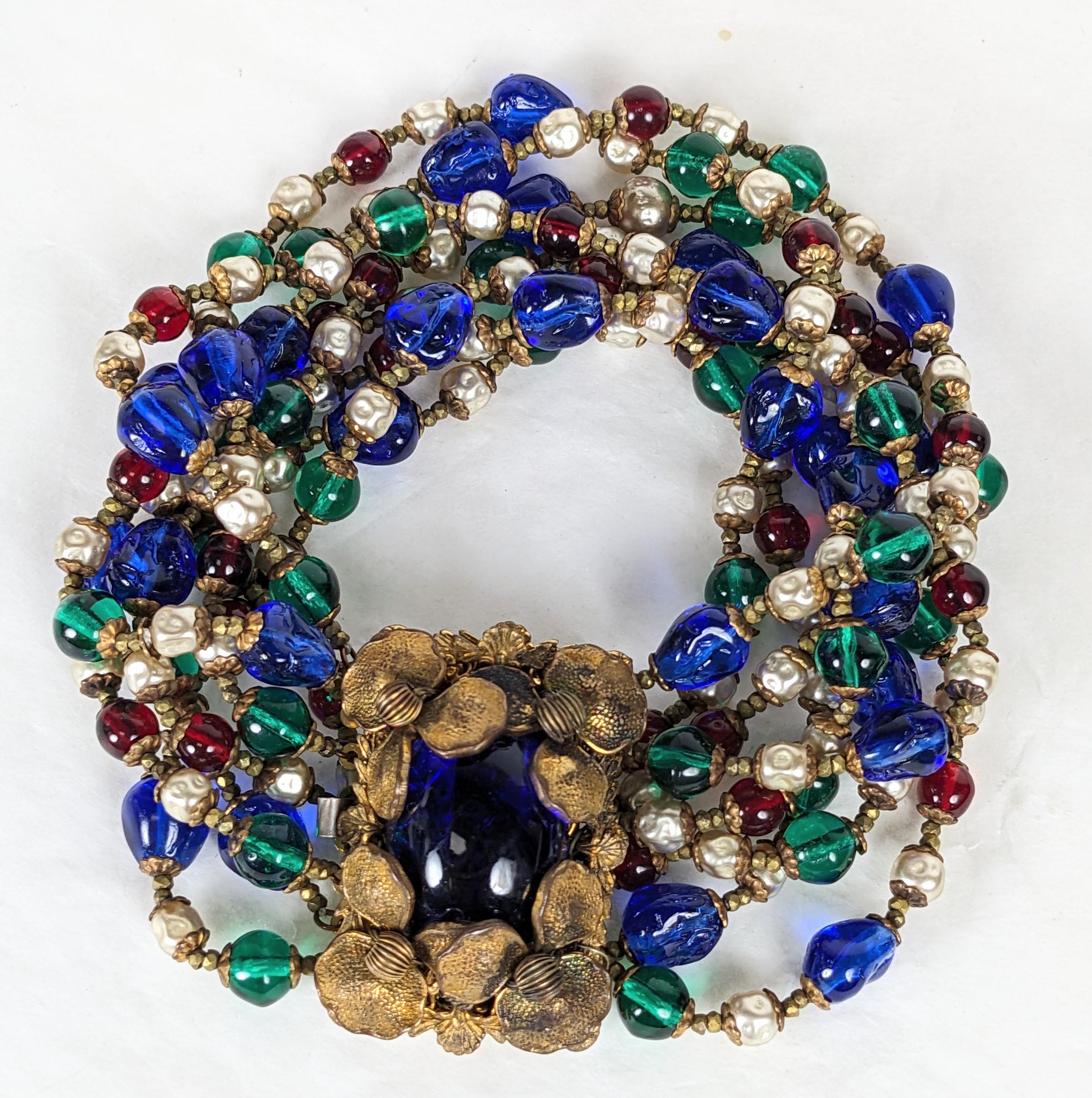 Incredibile bracciale di perline elaborato di Miriam Haskell degli anni '50. 8 fili di perle di vetro Gripoix fatte a mano nei colori smeraldo, rubino e zaffiro con finte perle e cappucci e accessori in oro russo. Ampia chiusura con grande zaffiro